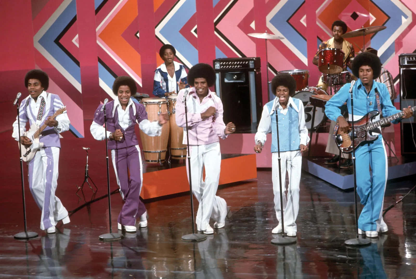 Young Michael Jackson 桌布 壁紙 — Jackson Five 在色彩繽紛的幾何舞台上充滿活力地表演，穿著鮮豔的70年代服裝，地板具有反射效果。
