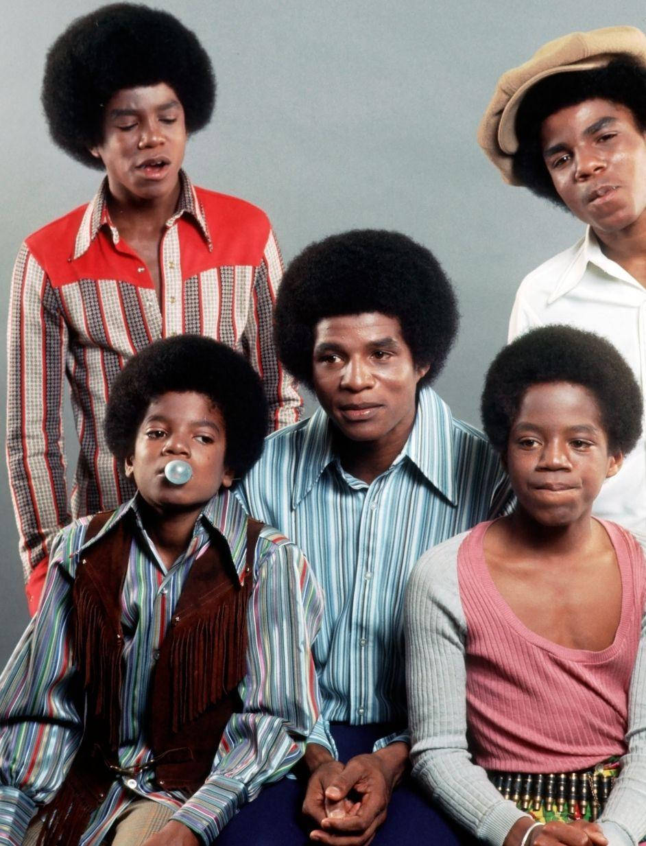 麥可·傑克森 桌布 壁紙 — Jackson Five 的五位成員穿著鮮豔的 1970 年代服裝，在純灰色工作室背景前擺姿勢。