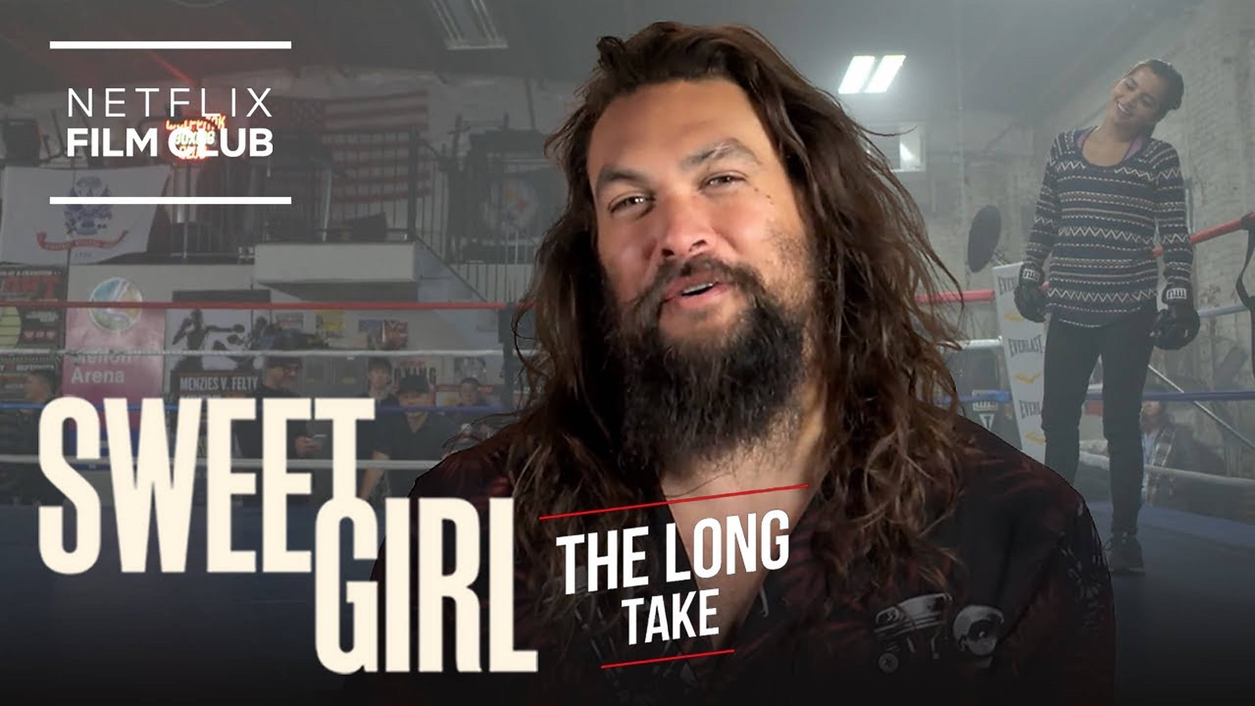 甜美女孩 桌布 壁紙 — Jason Momoa 留長髮和鬍鬚，在拳擊台上與一位女士交談，背景有 Netflix Film Club 品牌標誌。