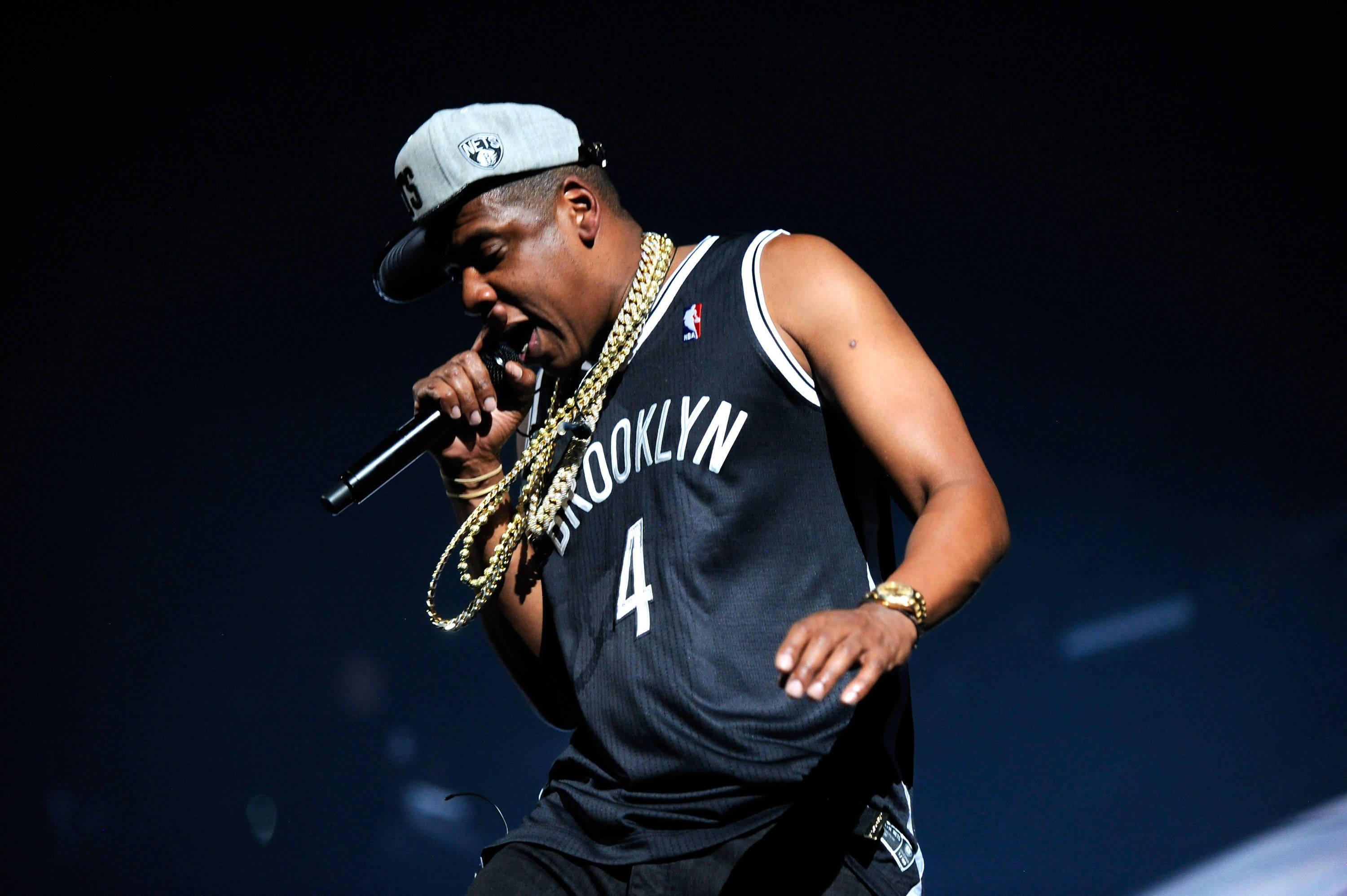 Jay-z 桌布 壁紙 — Jay Z 在舞台上熱情演出，身穿布魯克林球衣和金鏈，在戲劇性的藍色燈光下。