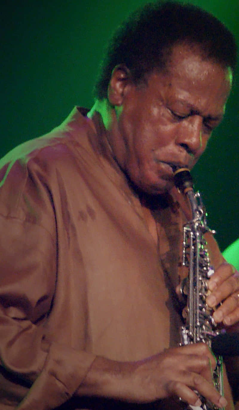 Wayne Shorter 桌布 壁紙 — 一位爵士薩克斯風手在綠色舞台燈光下充滿激情地演奏，神情專注，面部表情豐富。