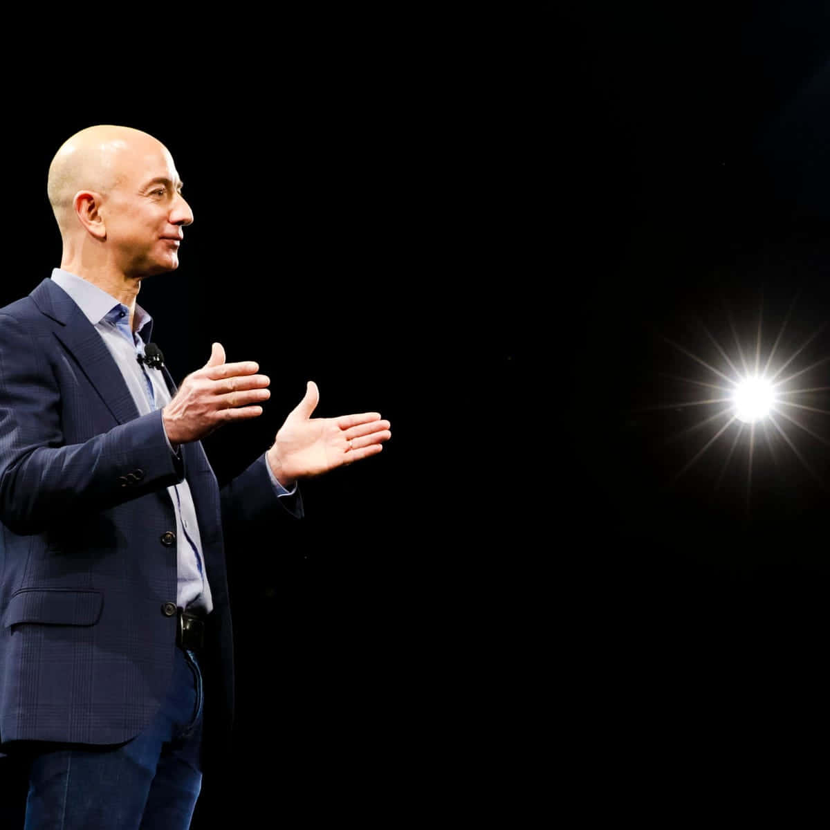 Jeff Bezos 桌布 壁紙 — Jeff Bezos 在一個被單一明亮聚光燈照亮的黑暗舞台上自信地做手勢。