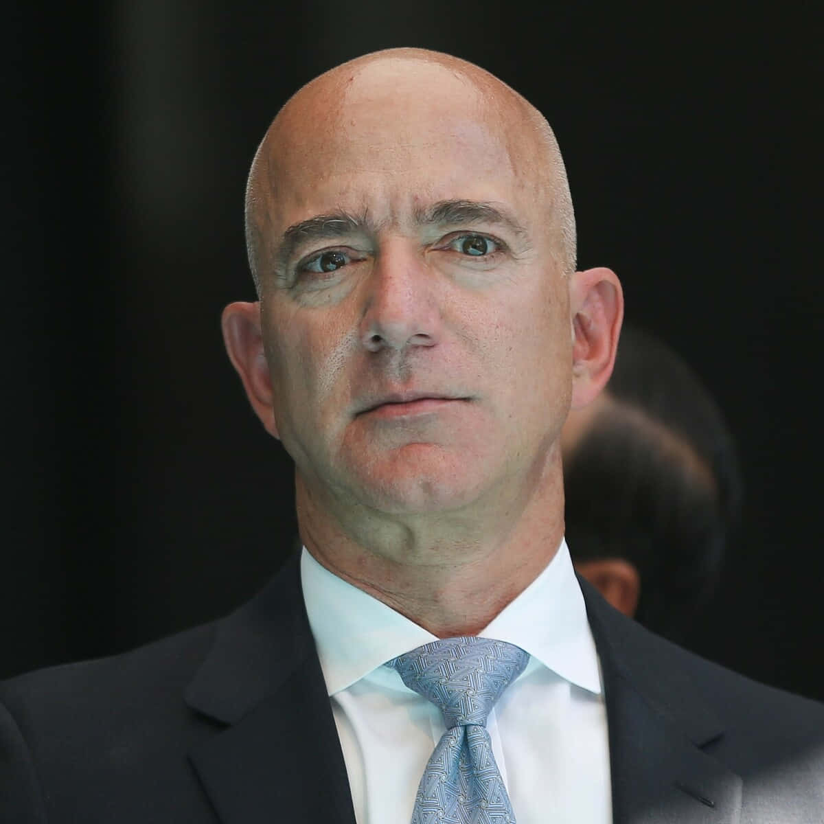 Jeff Bezos 桌布 壁紙 — Jeff Bezos 身穿深色西裝和圖案藍色領帶的頭像特寫，背景模糊深色。