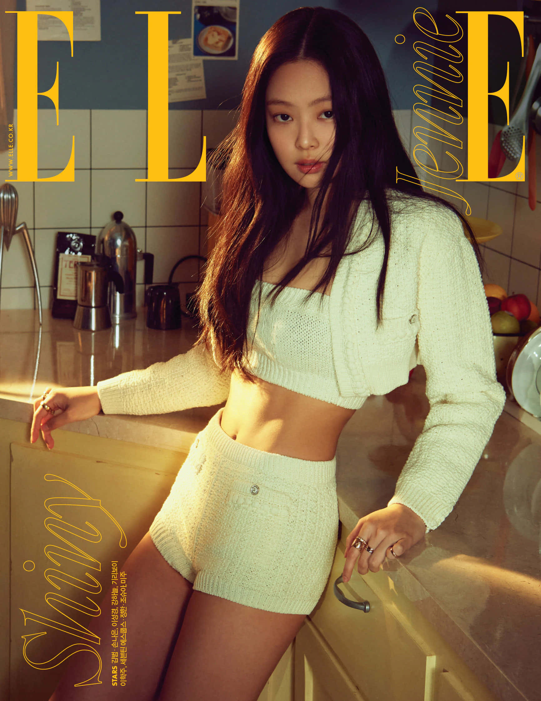 BLACKPINK 桌布 壁紙 — Jennie 自信地擺姿勢，身穿奶油色針織套裝，背景是溫暖的廚房，帶有金色燈光。