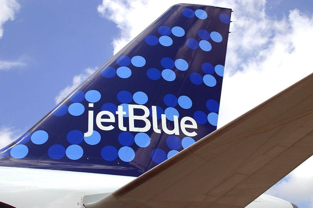  壁紙 — JetBlue 飛機尾翼特寫，帶有藍色波點，背景是明亮的藍天和蓬鬆的白雲。