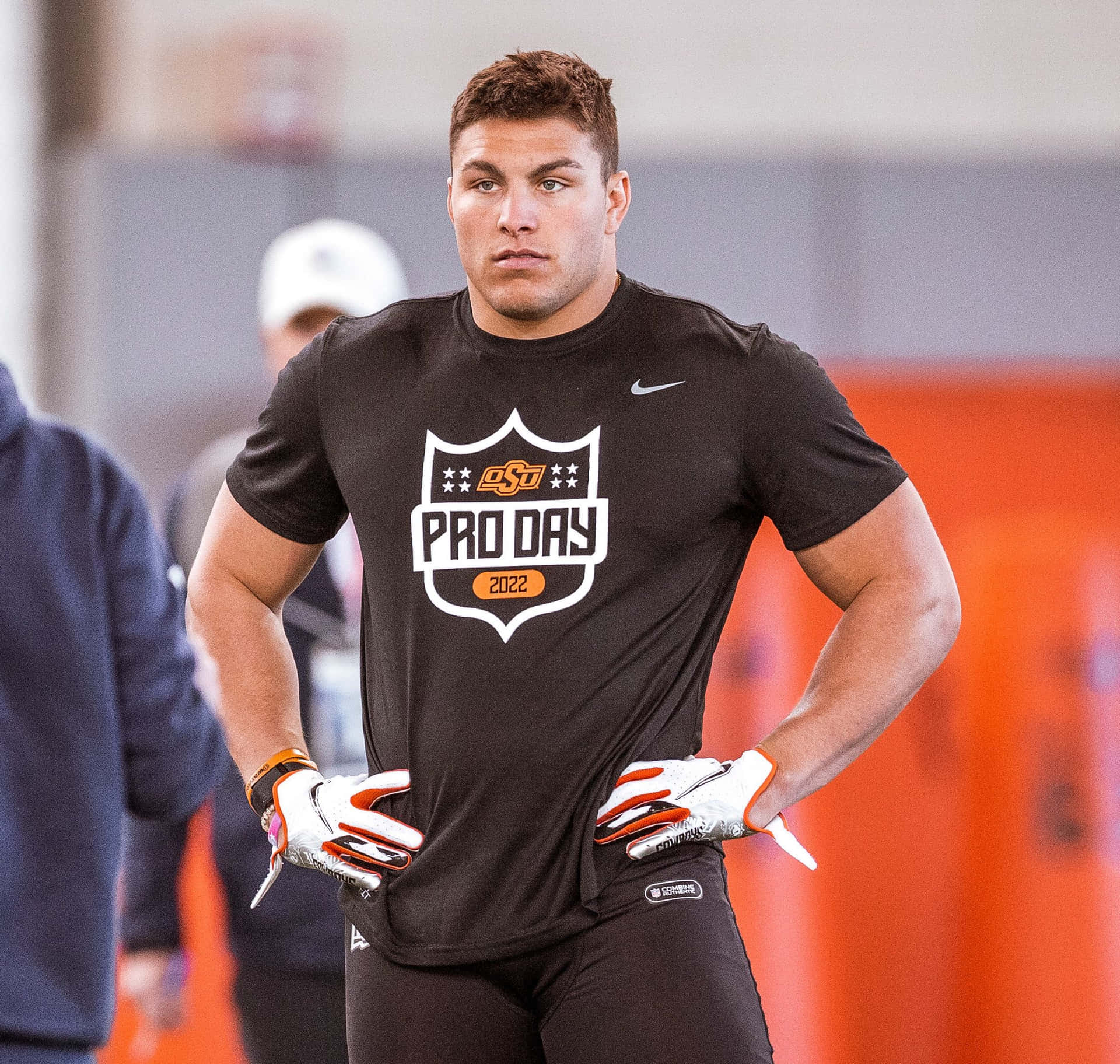  壁紙 — 一名肌肉發達的美式足球員穿著黑色 'OSU PRO DAY 2022' 上衣，在室內體育活動中自信地雙手叉腰站立。