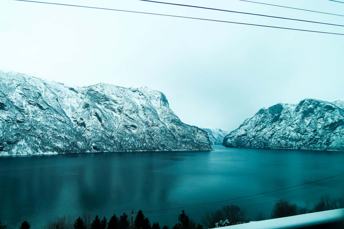  壁紙 — 積雪的山峰環繞著平靜的峽灣，天空多雲，電線橫跨畫面。