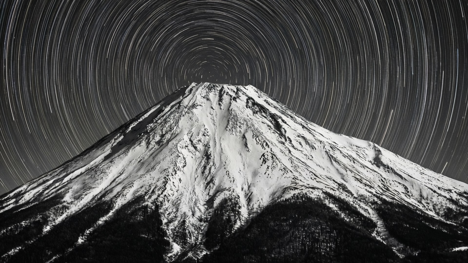 雪山 桌布 壁紙 — 積雪的山峰靜止不動，星星在夜空劃出圓形弧線，形成單色長時間曝光影像。