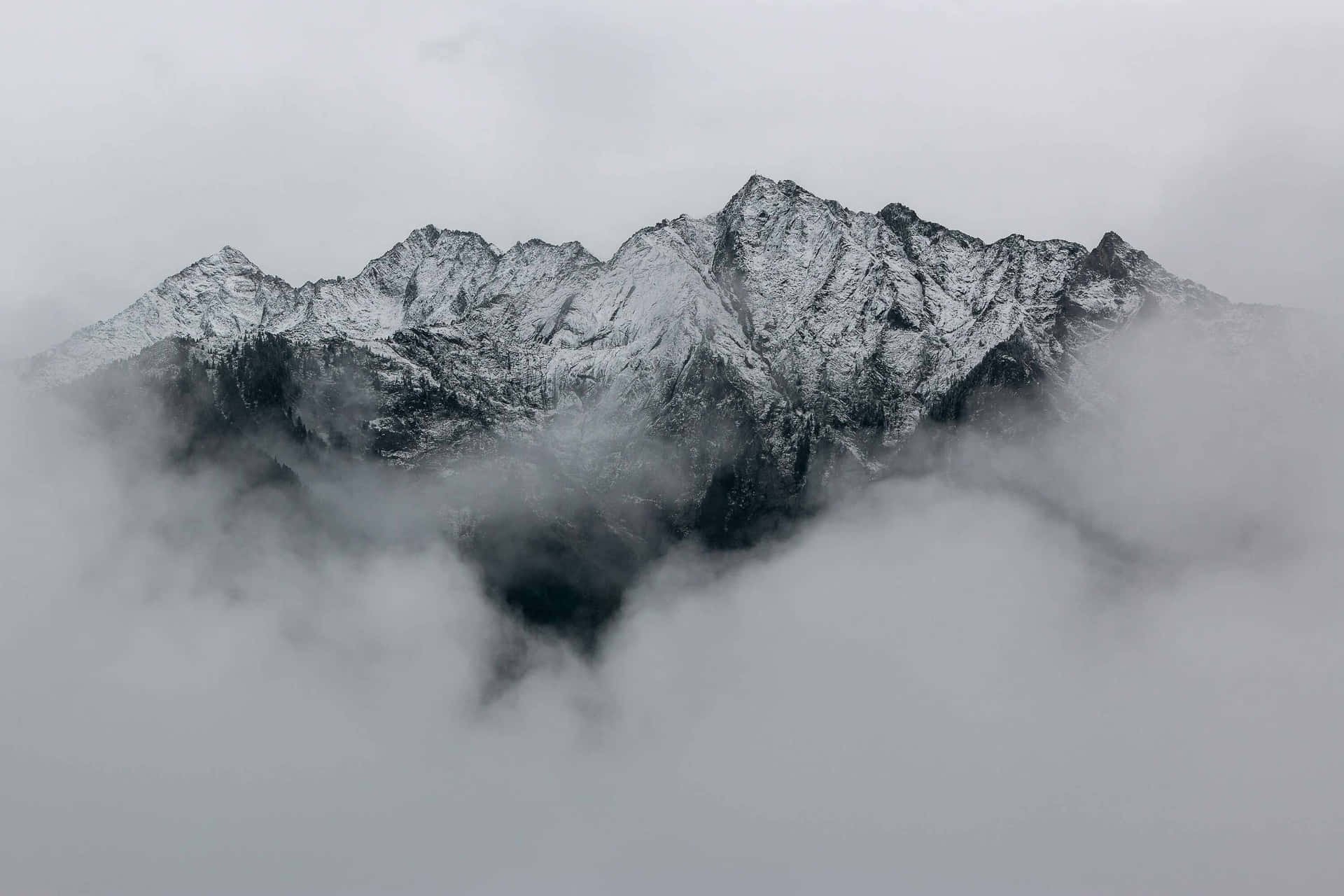  壁紙 — 積雪的山峰在陰天之下穿透濃霧。