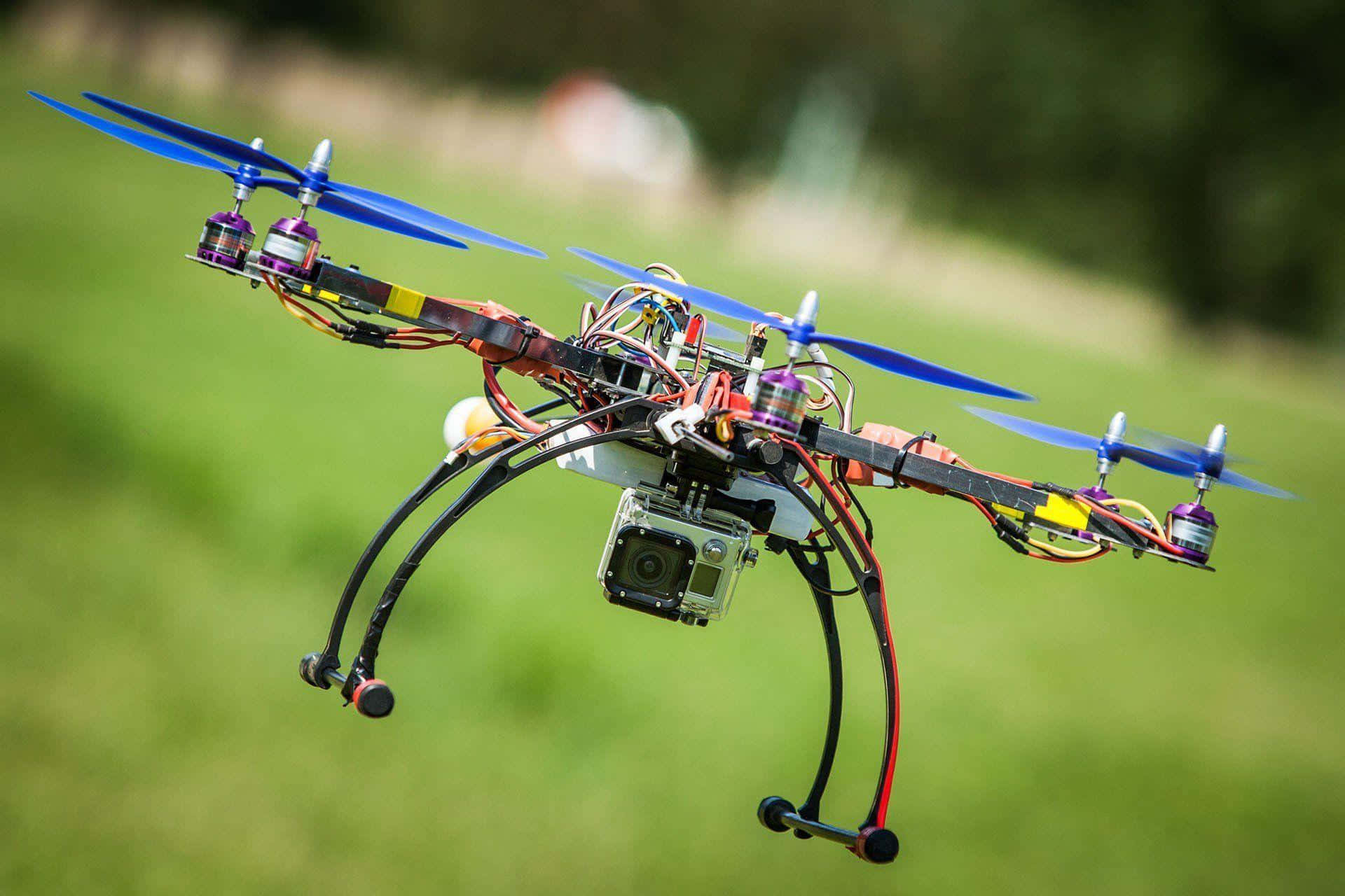 Drone Camera 桌布 壁紙 — 一架自訂建造的四軸無人機，帶有藍色螺旋槳，在明亮的日光下盤旋在茂密的綠色田野上空。