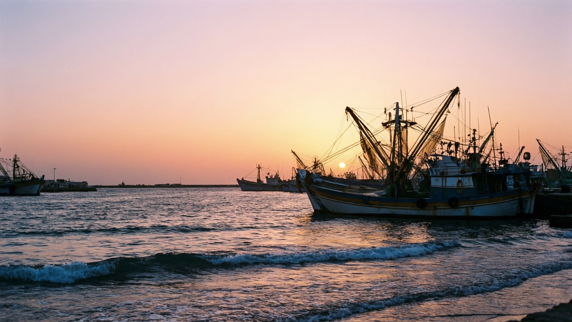Sunrise Fishing Harbor 壁紙 — 剪影的漁船在平靜的水面上休息，夕陽以溫暖的橙色和粉紅色調在地平線上落下。