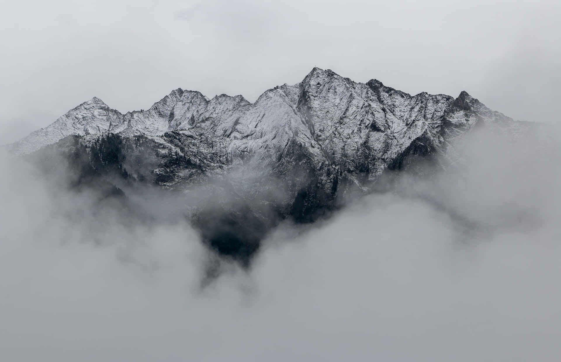 在陰天，積雪的山峰從濃密的雲層中浮現。 — Macbook Pro 壁紙