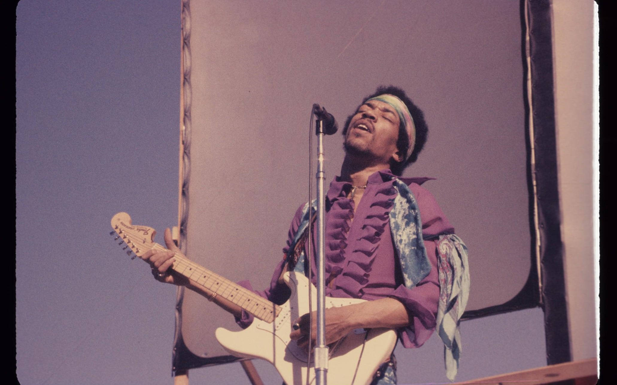 Celebrity 桌布 壁紙 — Jimi Hendrix 在紫色天空下，閉上眼睛，頭向後傾，熱情地在舞台上彈奏白色電吉他。