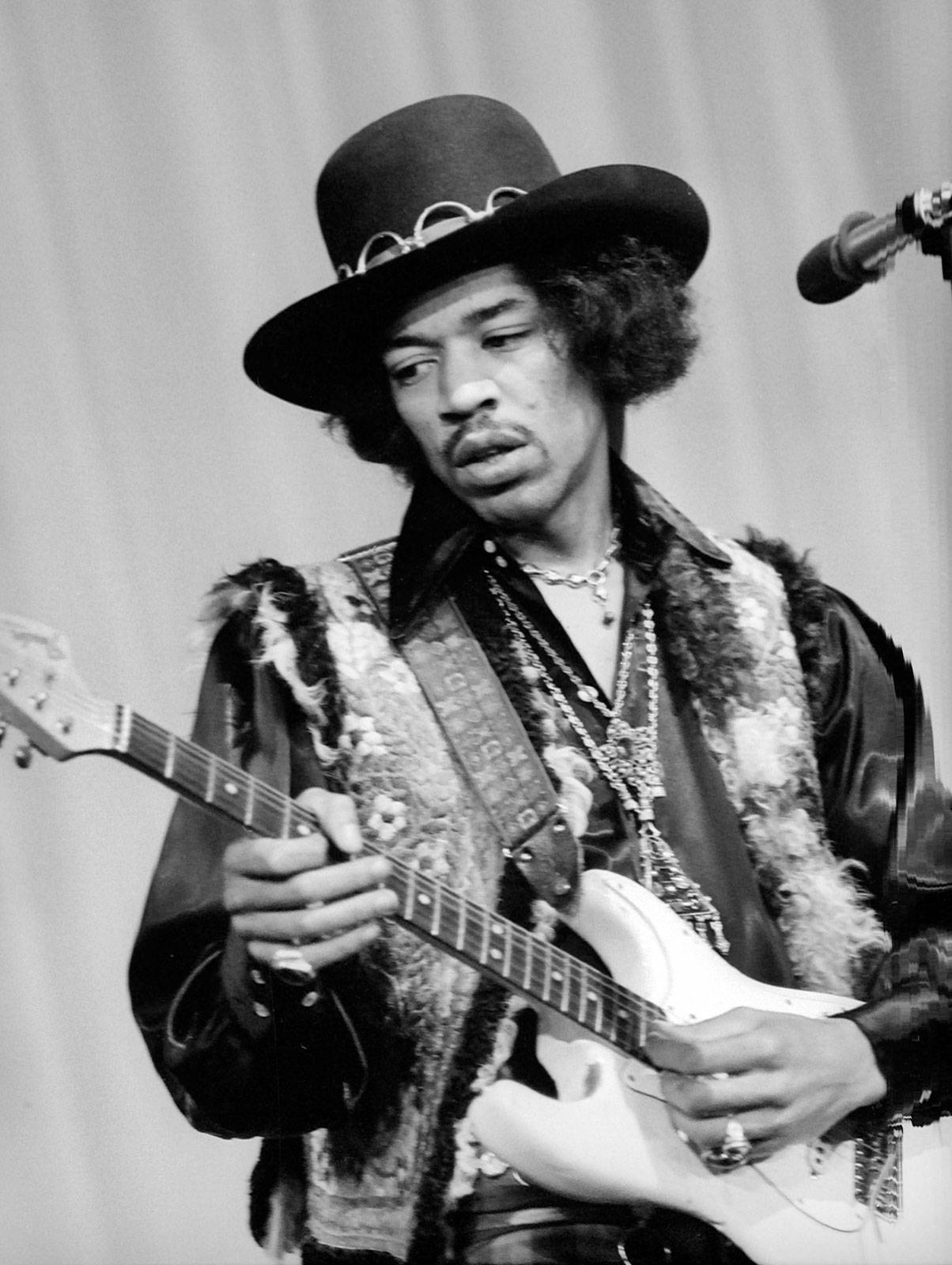 黑白 桌布 壁紙 — Jimi Hendrix 熱情地彈奏白色電吉他，戴著寬邊帽和層疊項鍊。