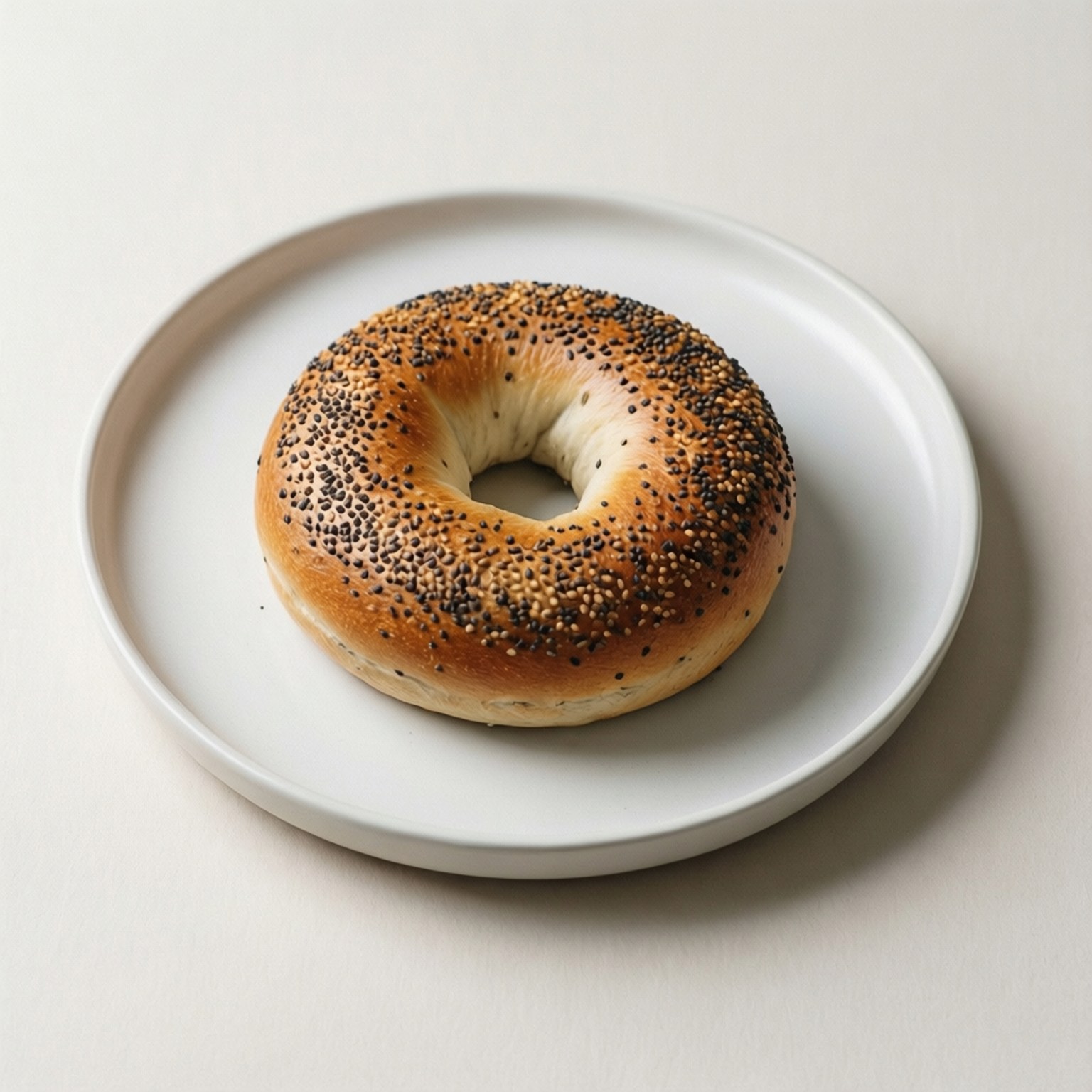 Minimalist Poppy Seed 壁紙 — 一個金黃色的貝果，上面撒有罌粟籽和芝麻，放在簡約的白色盤子中央，背景是柔和的米白色。