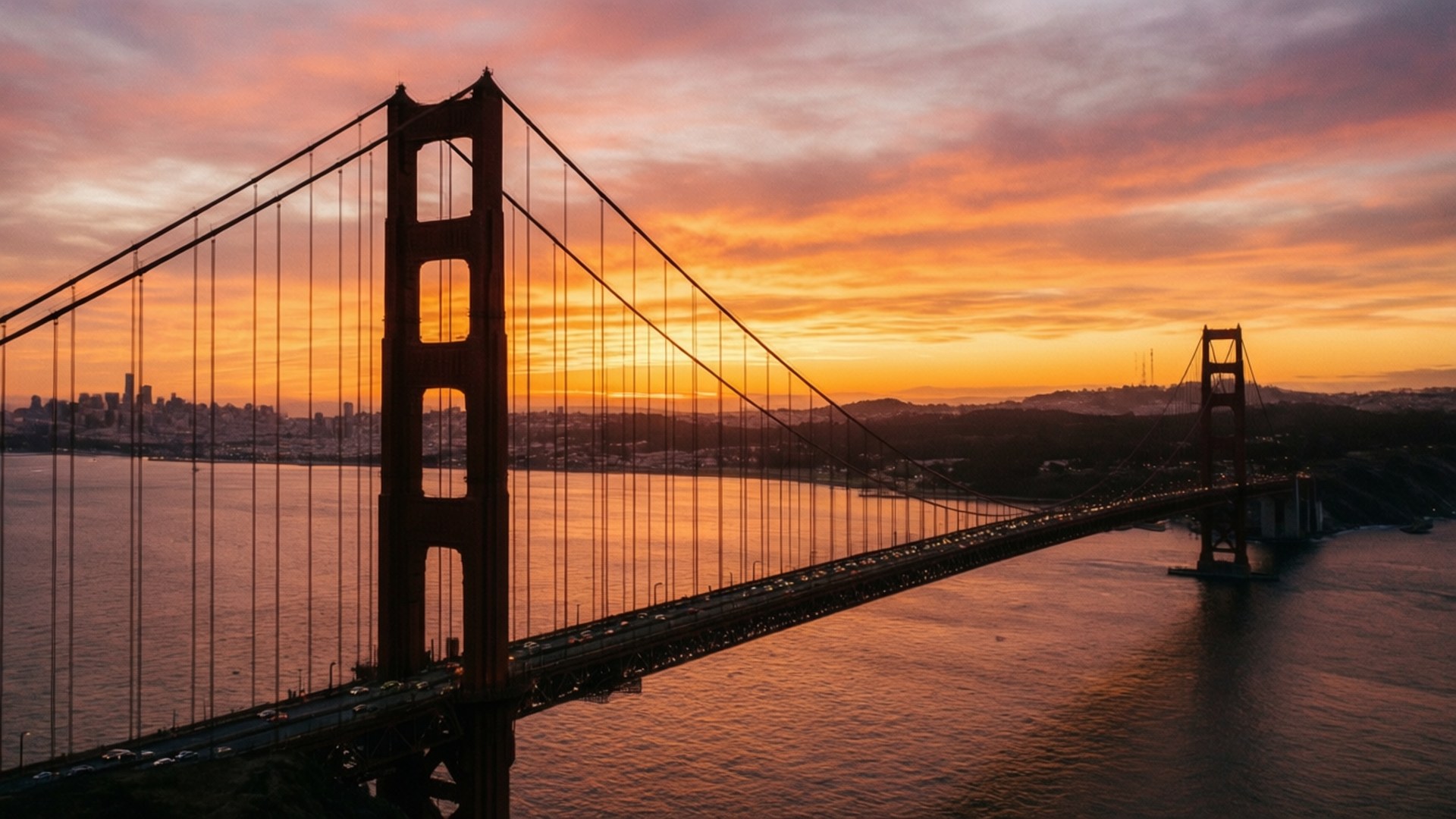 Golden Gate Sunset 壁紙 — 金門大橋在舊金山灣上空火熱的橙色和粉紅色日落映襯下形成剪影，遠處是城市天際線。