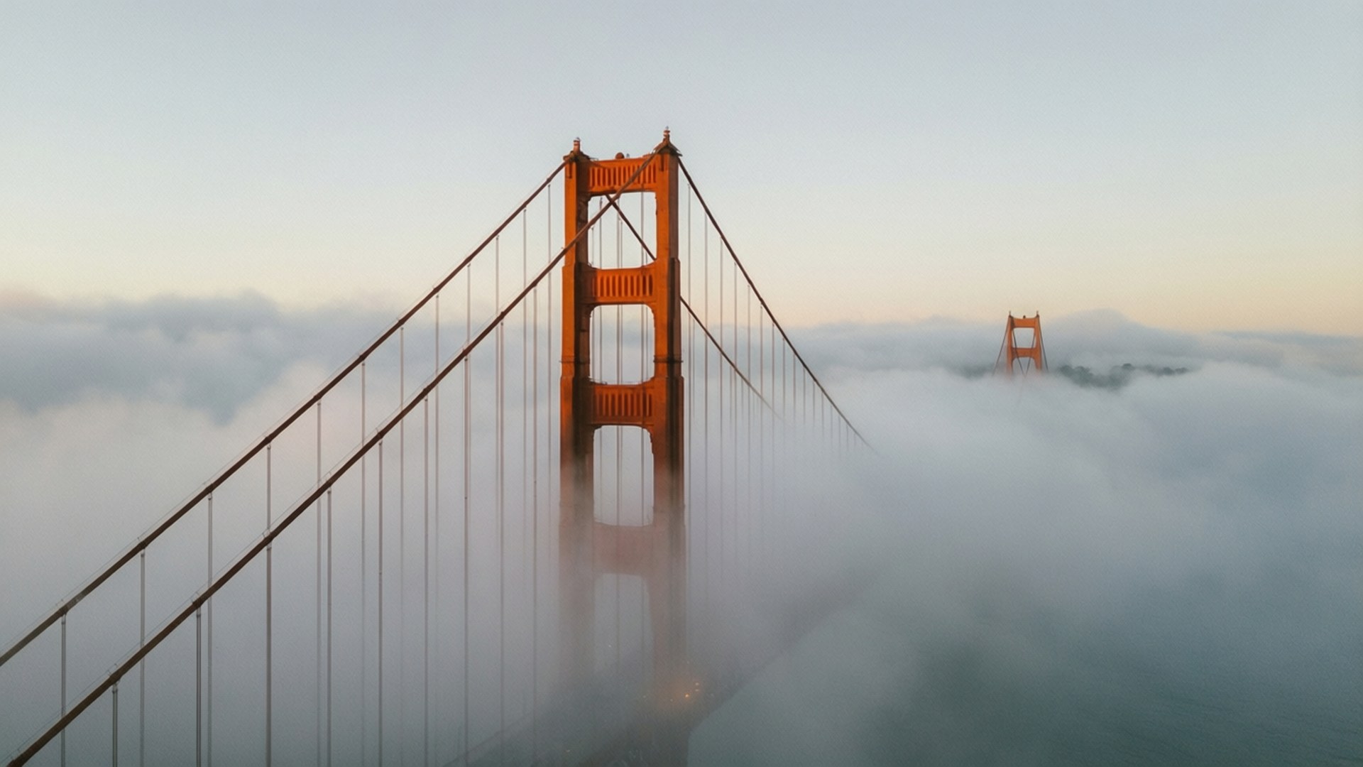 Golden Gate in Fog 壁紙 — 金門大橋在黎明時分從濃霧中浮現，上方是柔和的粉彩天空。