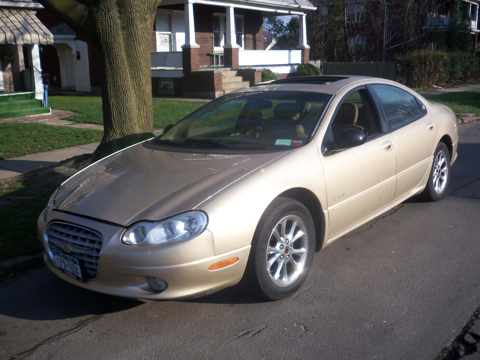 Chrysler Lhs 桌布 壁紙 — 一輛金色轎車停放在住宅街道旁，旁邊有樹，背景有房屋。