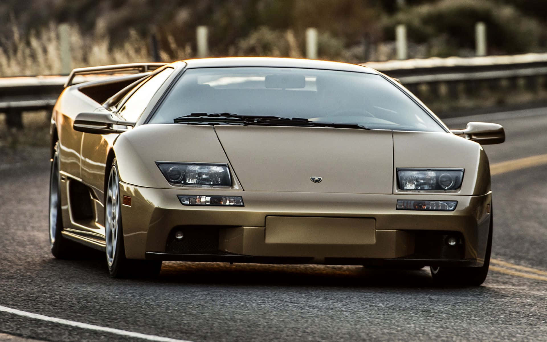Lamborghini Diablo 桌布 壁紙 — 一輛金色藍寶堅尼Diablo跑車在陽光明媚的高速公路上閃閃發光，路邊植物模糊。