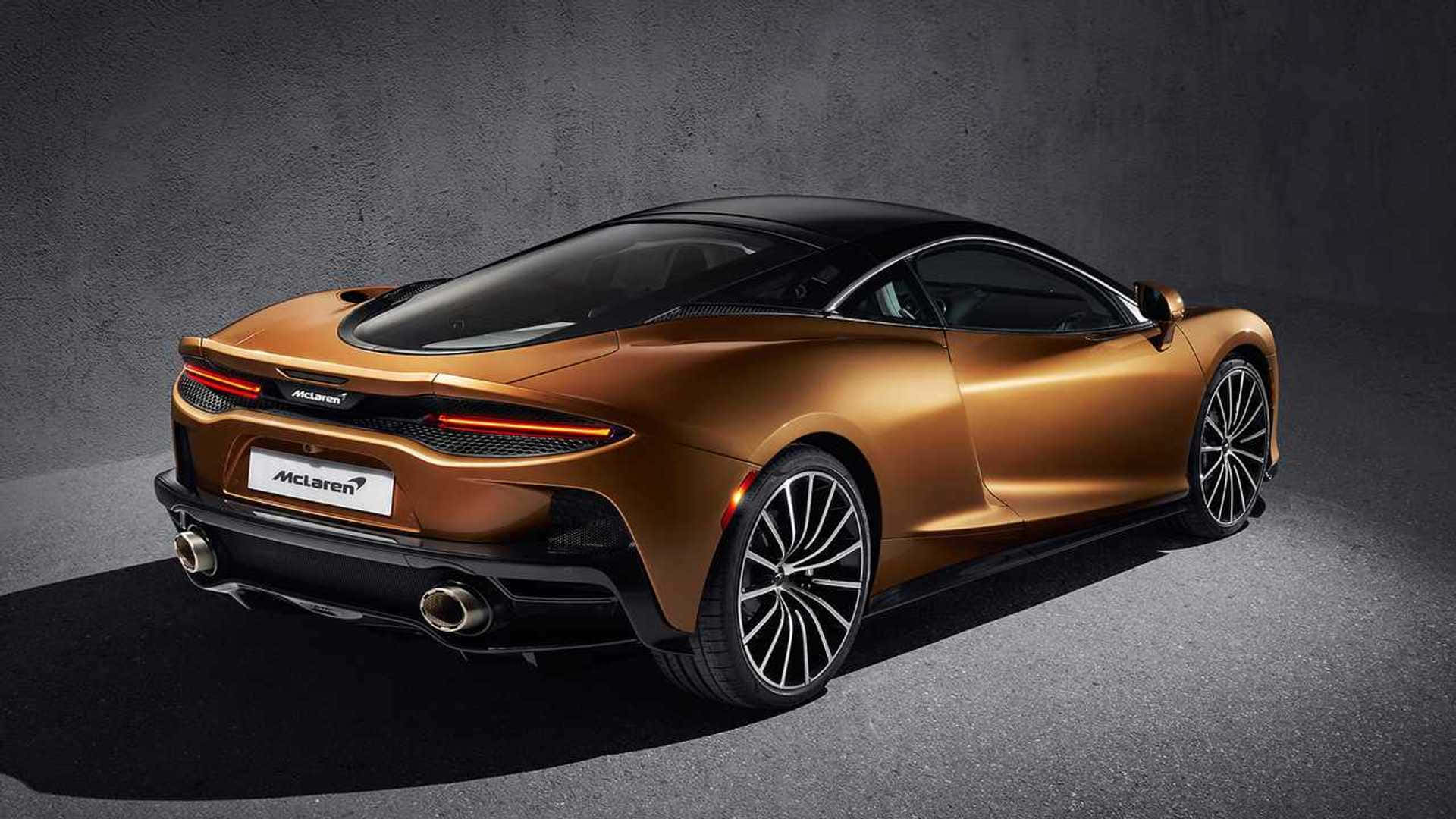 Mclaren Gt 桌布 壁紙 — 一輛時尚的金色McLaren跑車，帶有黑色飾邊和發光的尾燈，在深色紋理工作室牆前展示。