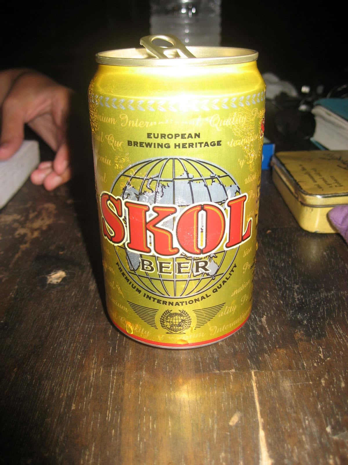  壁紙 — 一個金色Skol啤酒罐，上面有紅色字樣，放在昏暗燈光下的深色木桌上。