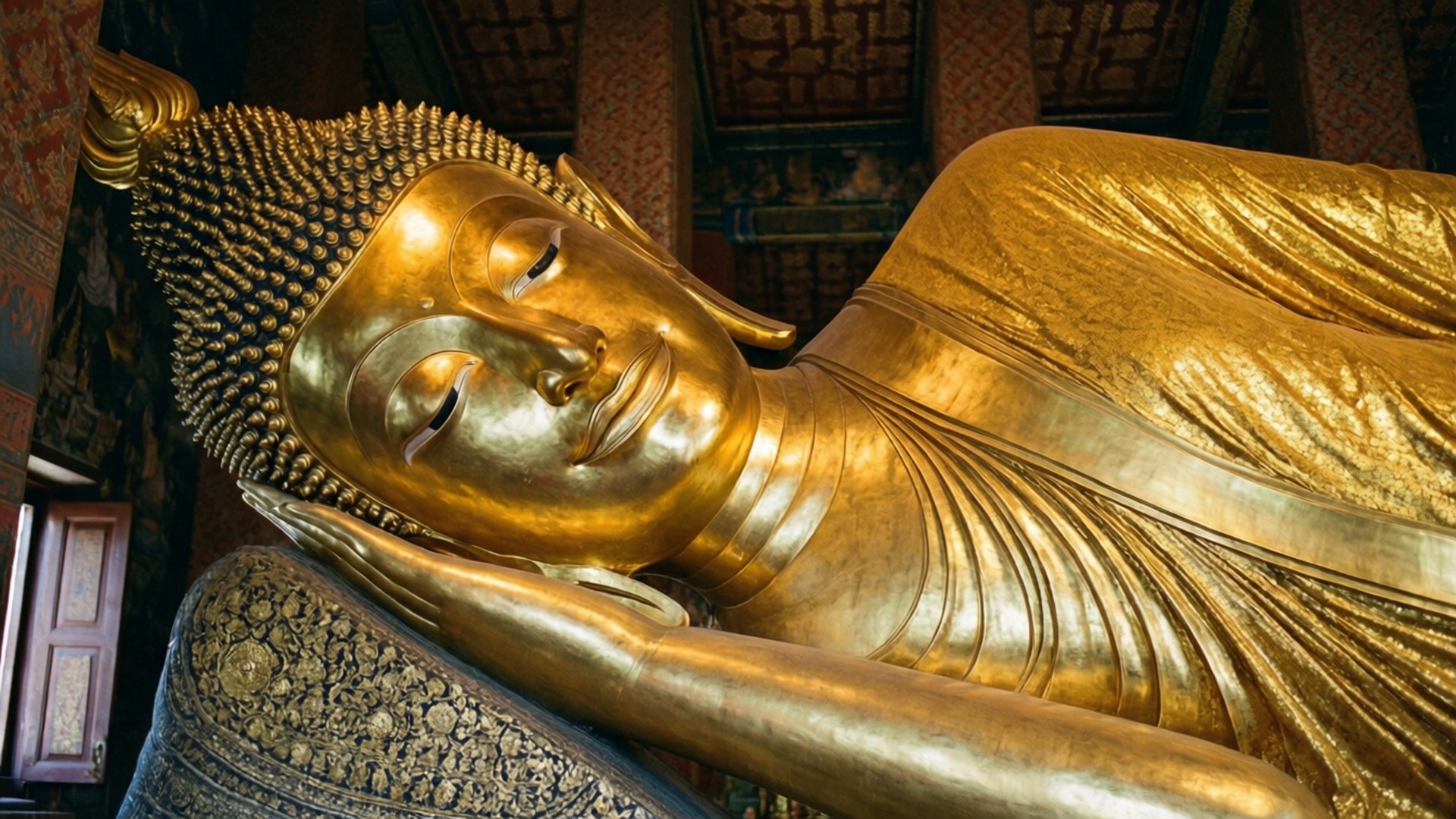 Reclining Peaceful Buddha 壁紙 — 一座寧靜的金色臥佛雕像安詳地躺在寺廟內裝飾華麗的墊子上，寺廟有精緻的木樑。