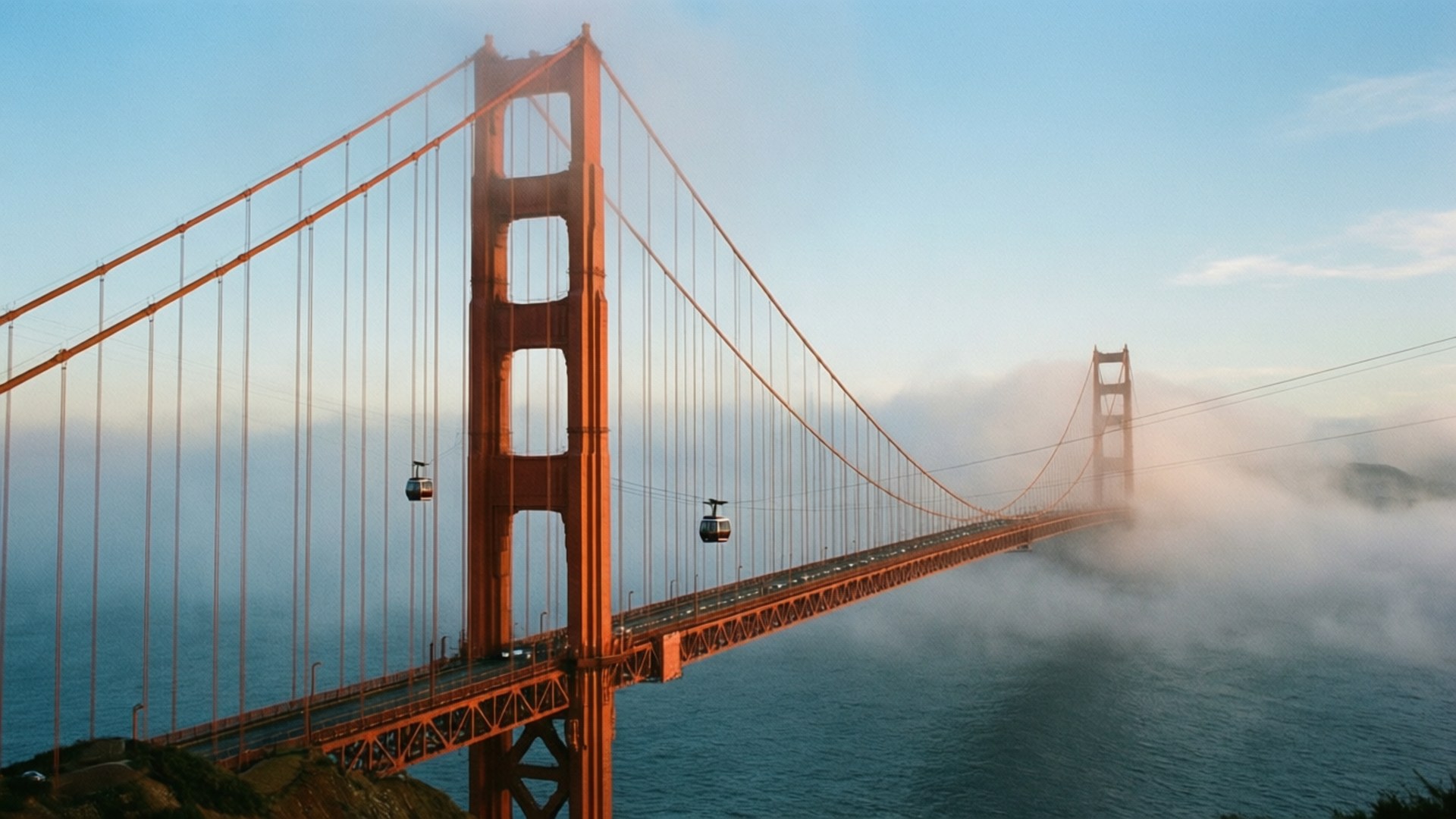 Foggy Golden Gate 壁紙 — 金門大橋在溫暖的橙色中雄偉地聳立，襯著柔和的藍天，霧氣在橋塔下方翻滾。