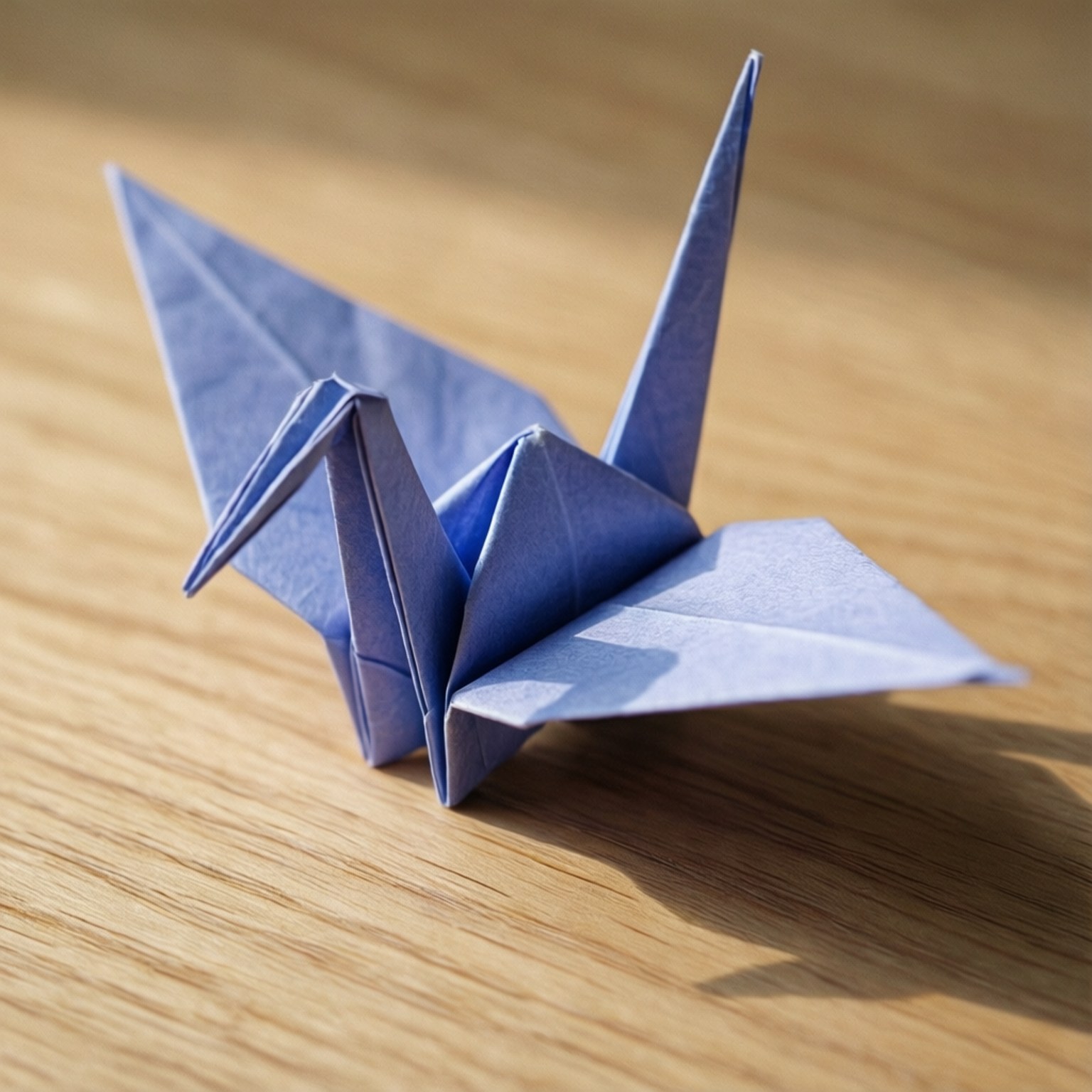 Periwinkle Origami Crane 壁紙 — 一隻精緻的藍色摺紙鶴佇立在溫暖的木質表面上，沐浴在柔和自然光中。