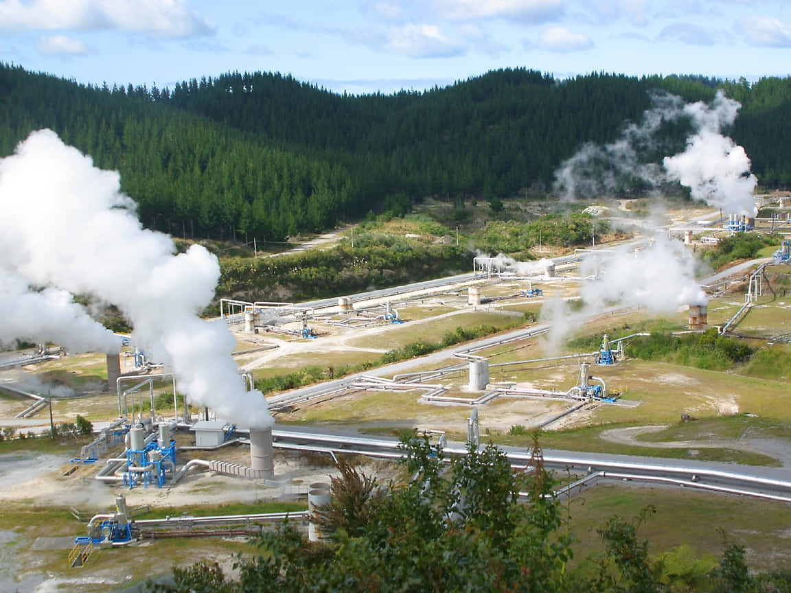  壁紙 — 蒸氣從位於森林山谷中的地熱發電廠管道升起，天空部分多雲。