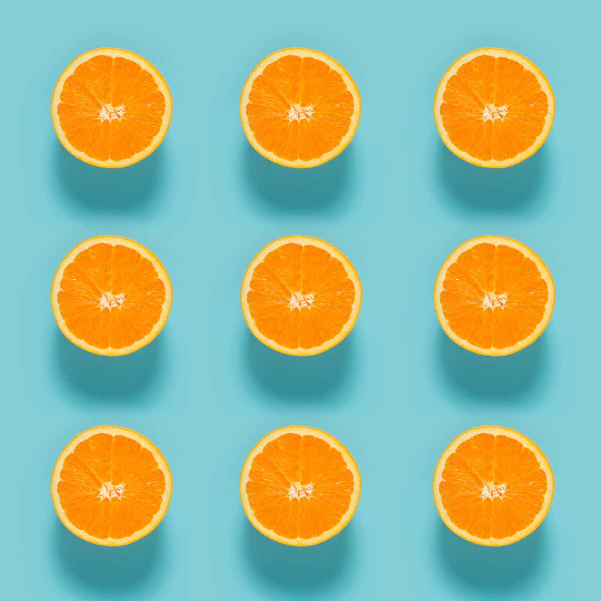 Orange And Blue 桌布 壁紙 — 九個鮮豔的橙半邊整齊排列在明亮的青色背景上，帶有柔和陰影。