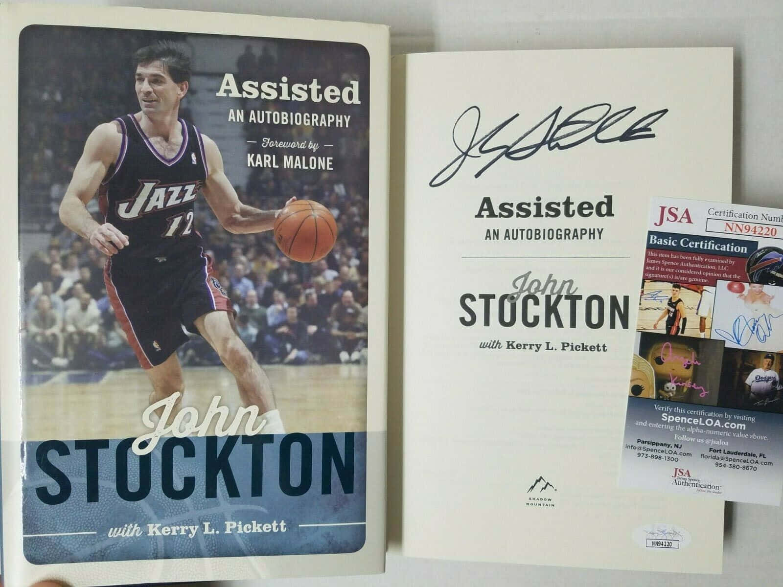 NBA 桌布 壁紙 — John Stockton 的自傳《Assisted》簽名本，附有JSA認證貼紙，展示在書封旁邊。