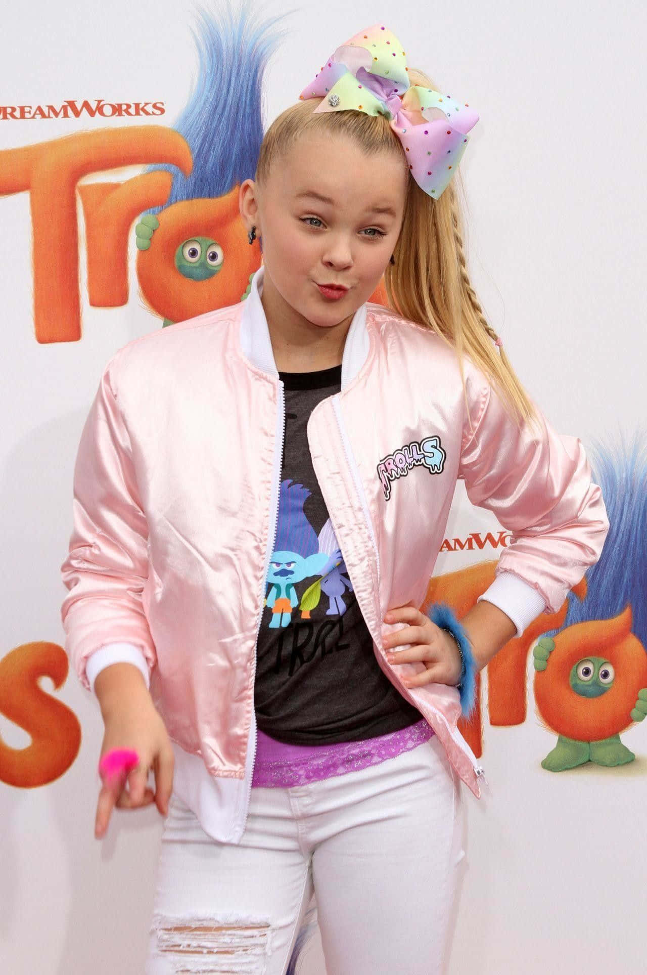 Jojo 桌布 壁紙 — JoJo Siwa 自信地穿著粉紅色 bomber 外套和白色破洞牛仔褲，在 DreamWorks Trolls 宣傳背景前擺姿勢。