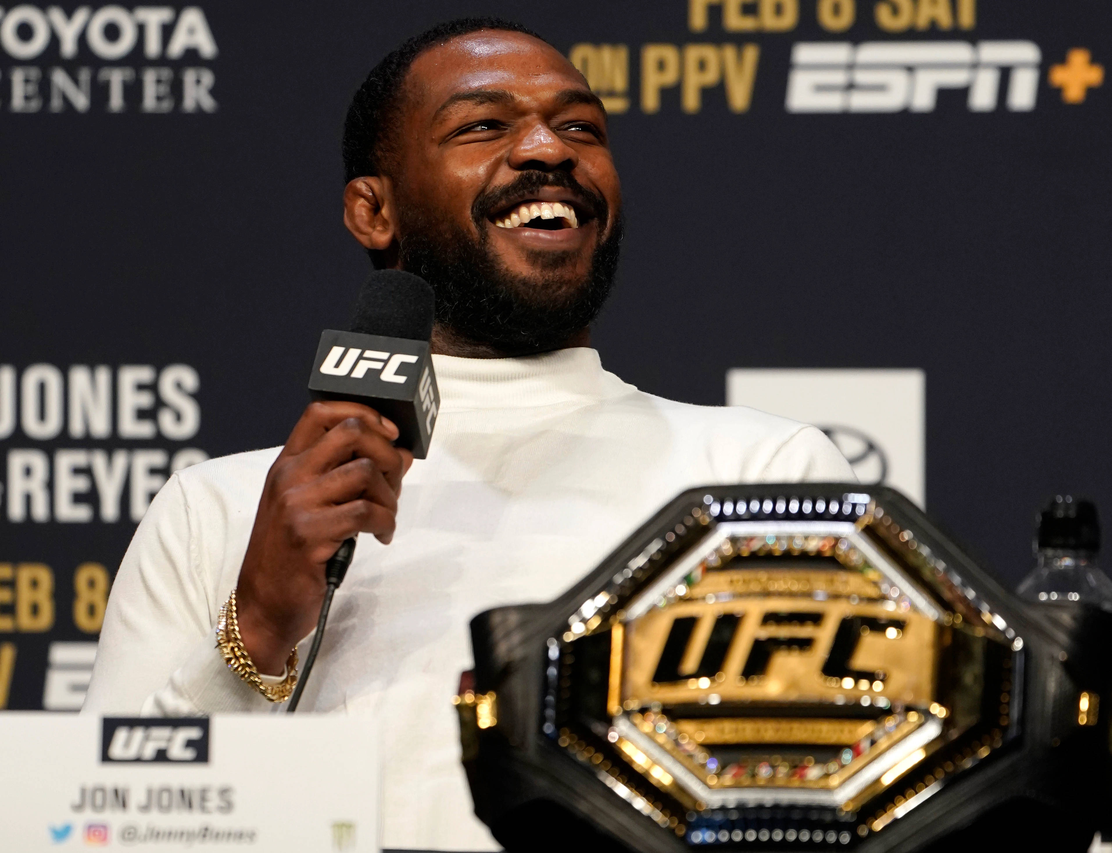 白色 桌布 壁紙 — Jon Jones 在ESPN品牌背景的記者會上，手持UFC冠軍腰帶，滿面笑容。