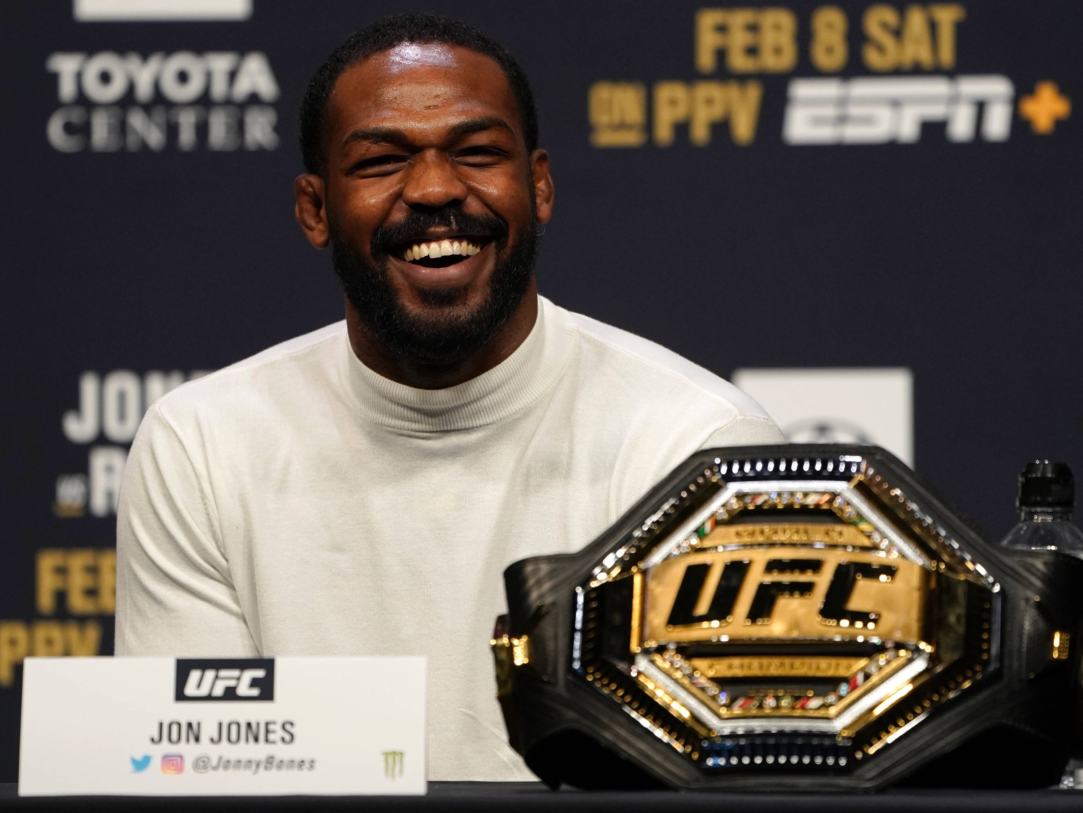 Champion 桌布 壁紙 — Jon Jones 在記者會上自豪地微笑，身旁是閃閃發光的UFC冠軍腰帶。