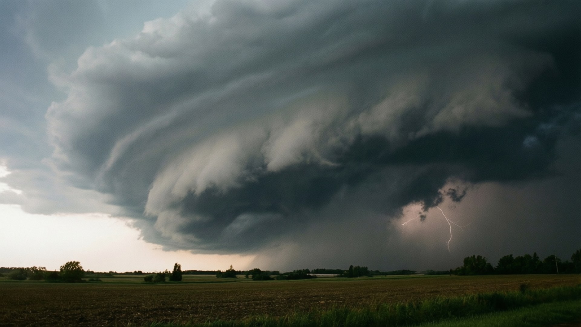 Grey Storm Clouds 壁紙 — 巨大的黑暗風暴雲籠罩在平坦的田野上，閃電在其底部閃爍。