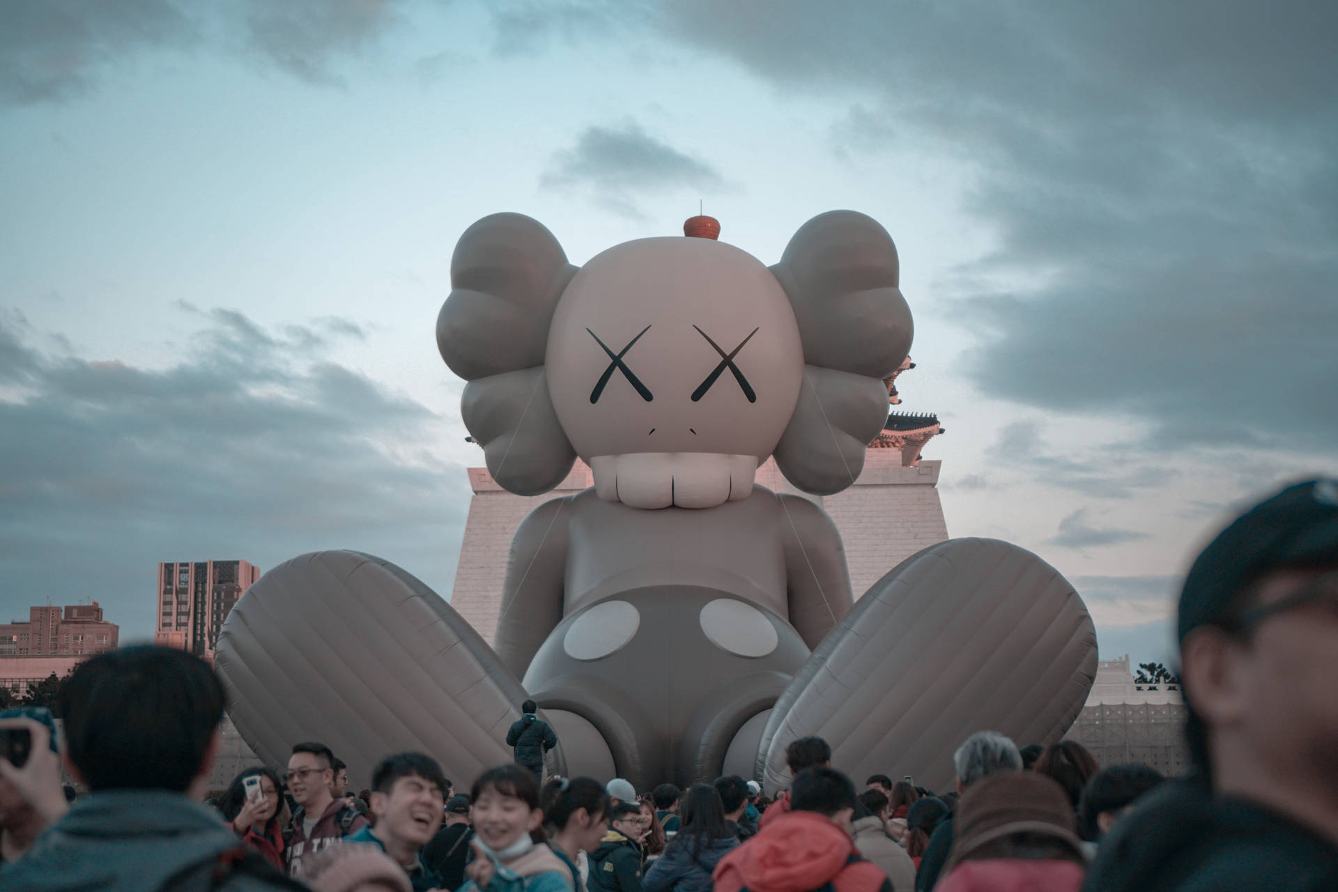 人群在暮色中聚集在巨大的KAWS氣球周圍。 — Kaws 壁紙
