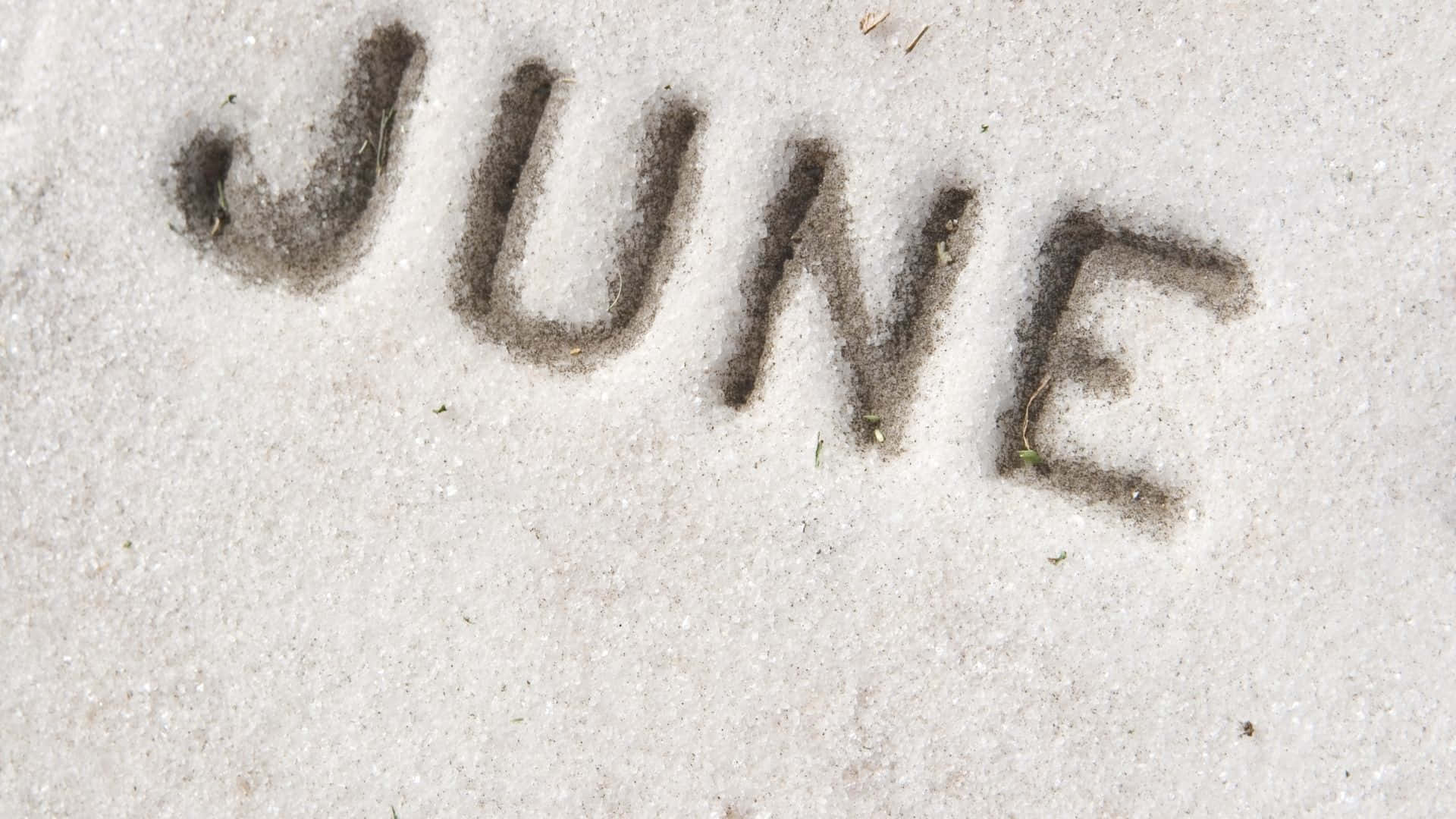 June 桌布 壁紙 — 「JUNE」這個字用深色沙寫在淺色紋理的沙灘表面。