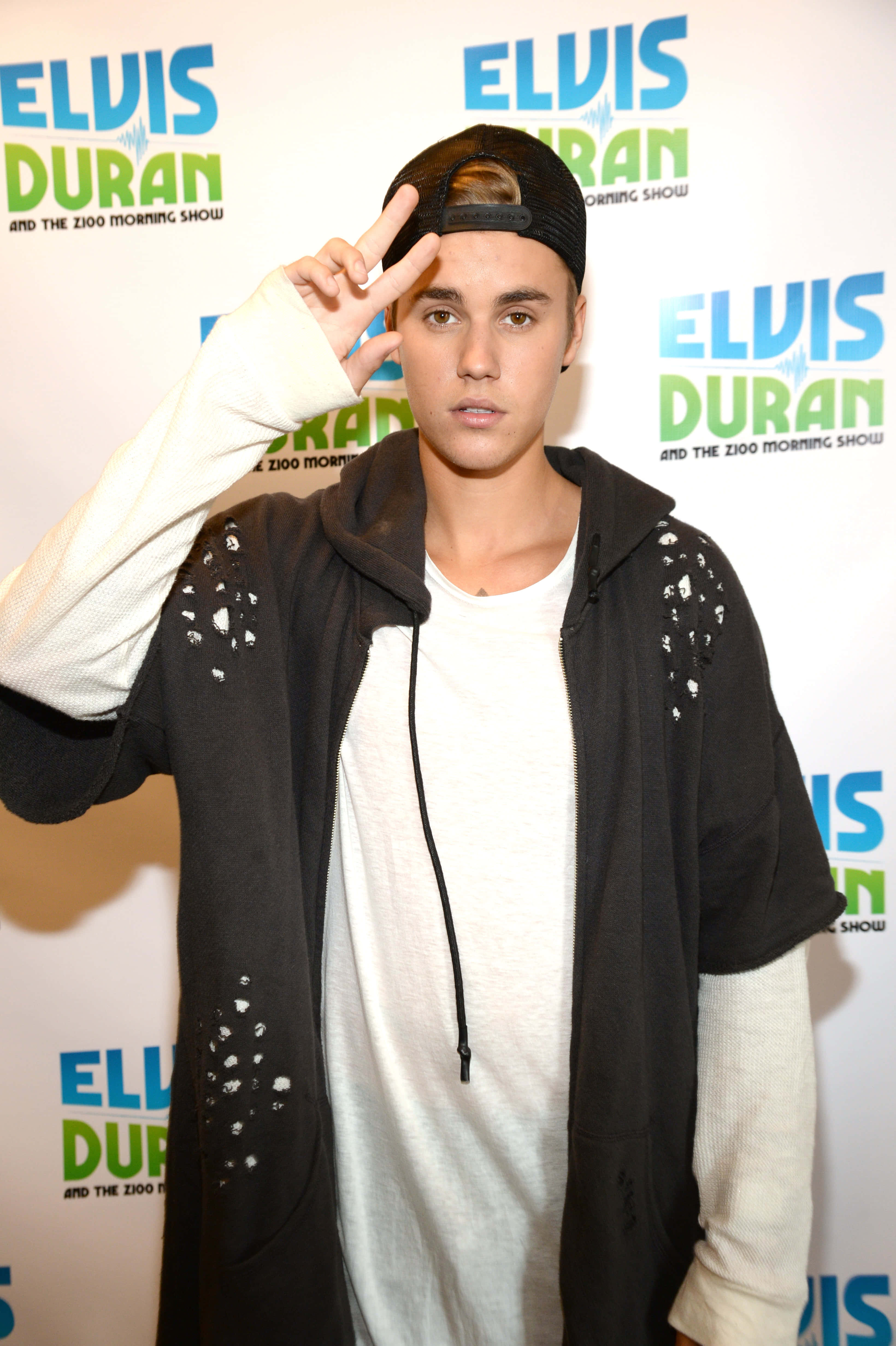 Justin Bieber 2015 桌布 壁紙 — Justin Bieber 在 Elvis Duran 電台節目活動中擺出和平手勢，身穿黑色連帽衫和向後戴的帽子。
