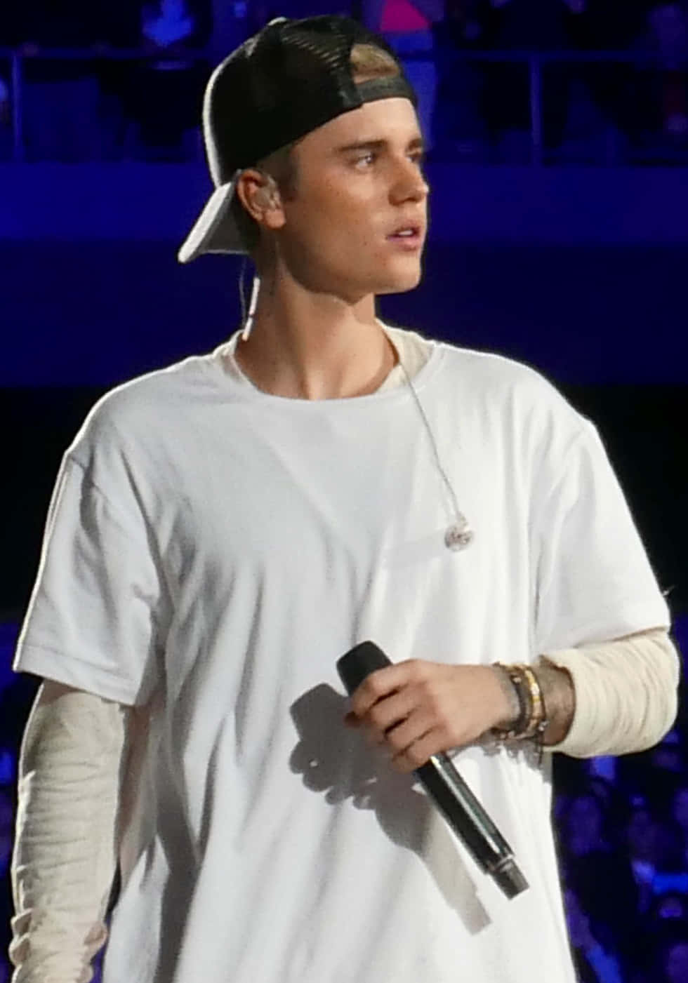 Justin Bieber 2015 桌布 壁紙 — Justin Bieber 在舞台上表演，身穿白色T恤和黑色帽子，在藍色舞台燈光下拿著麥克風。