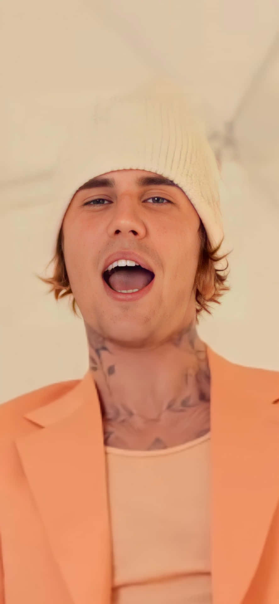 Justin Bieber 2021 桌布 壁紙 — Justin Bieber 穿著蜜桃色西裝外套和奶油色毛帽，在柔和的米色背景下深情演唱。