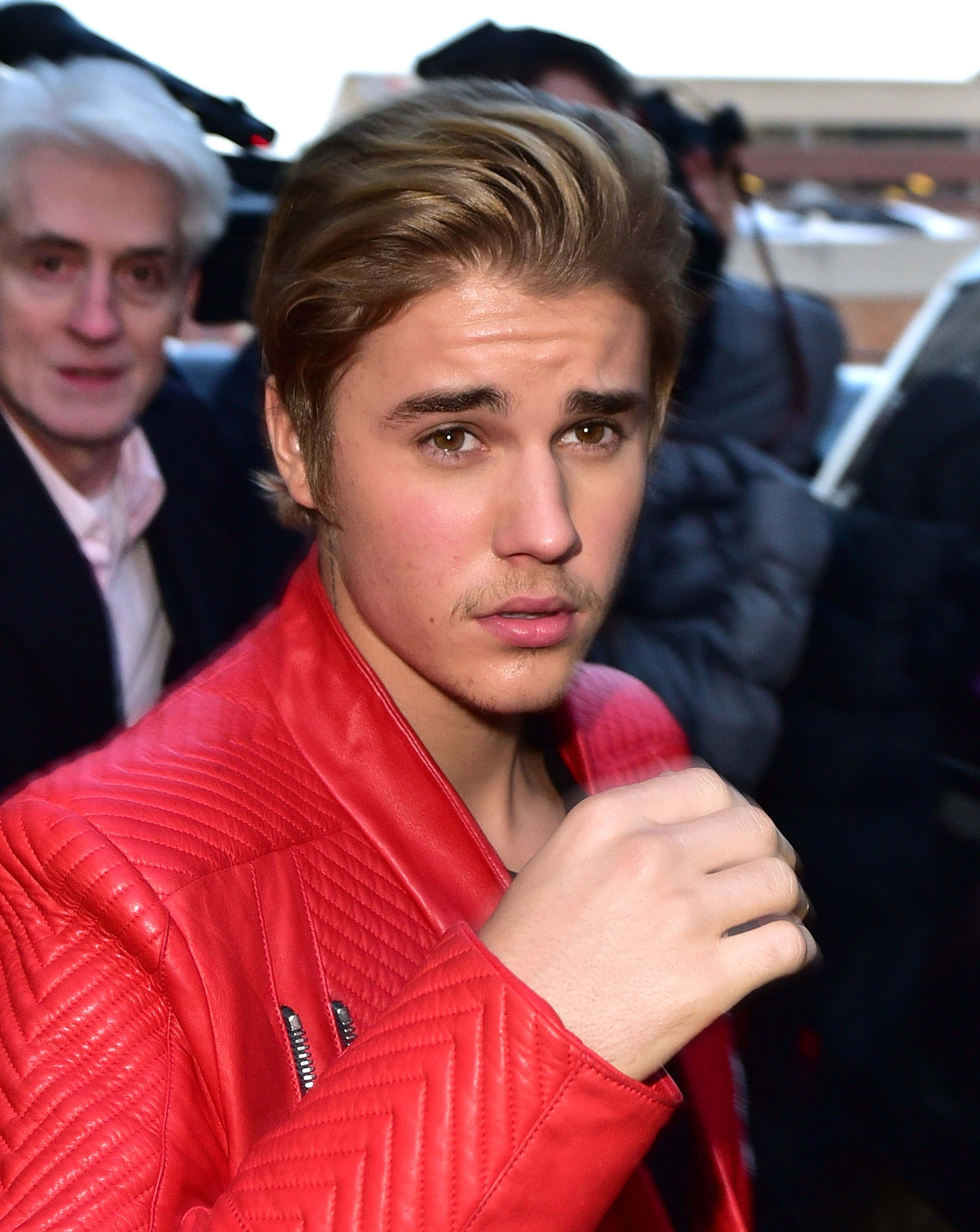 Justin Bieber 2015 桌布 壁紙 — Justin Bieber 穿著一件大膽的紅色絎縫皮革外套，在狗仔隊包圍下，表情嚴肅地直視鏡頭。