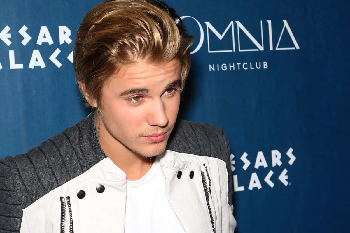 Justin Bieber 2015 桌布 壁紙 — Justin Bieber 穿著白色和灰色外套，在藍色品牌背景前望向鏡頭外。