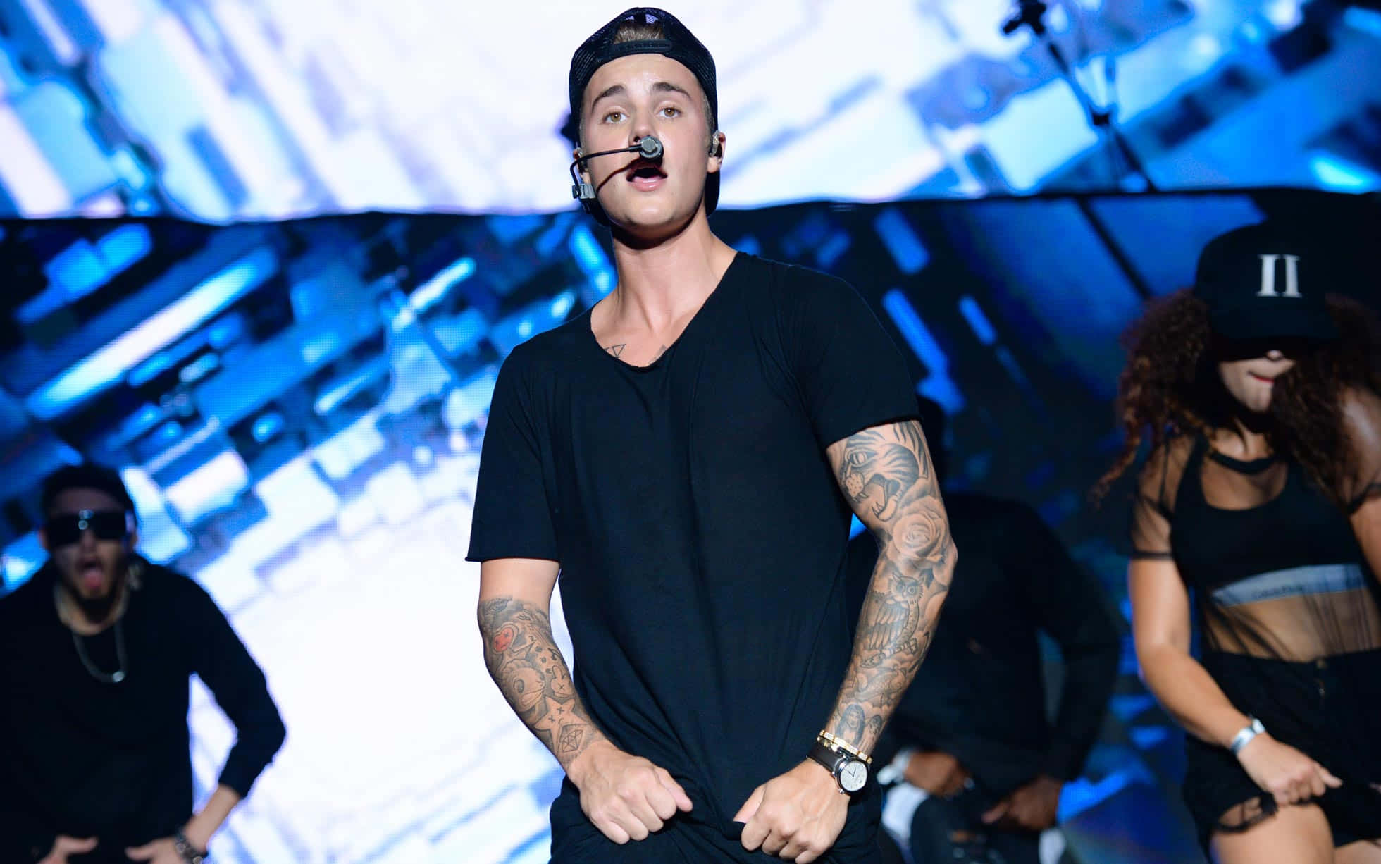 Justin Bieber 2015 桌布 壁紙 — Justin Bieber 身穿黑色服裝在舞台上表演，在明亮的藍色舞台燈光下可見刺青。