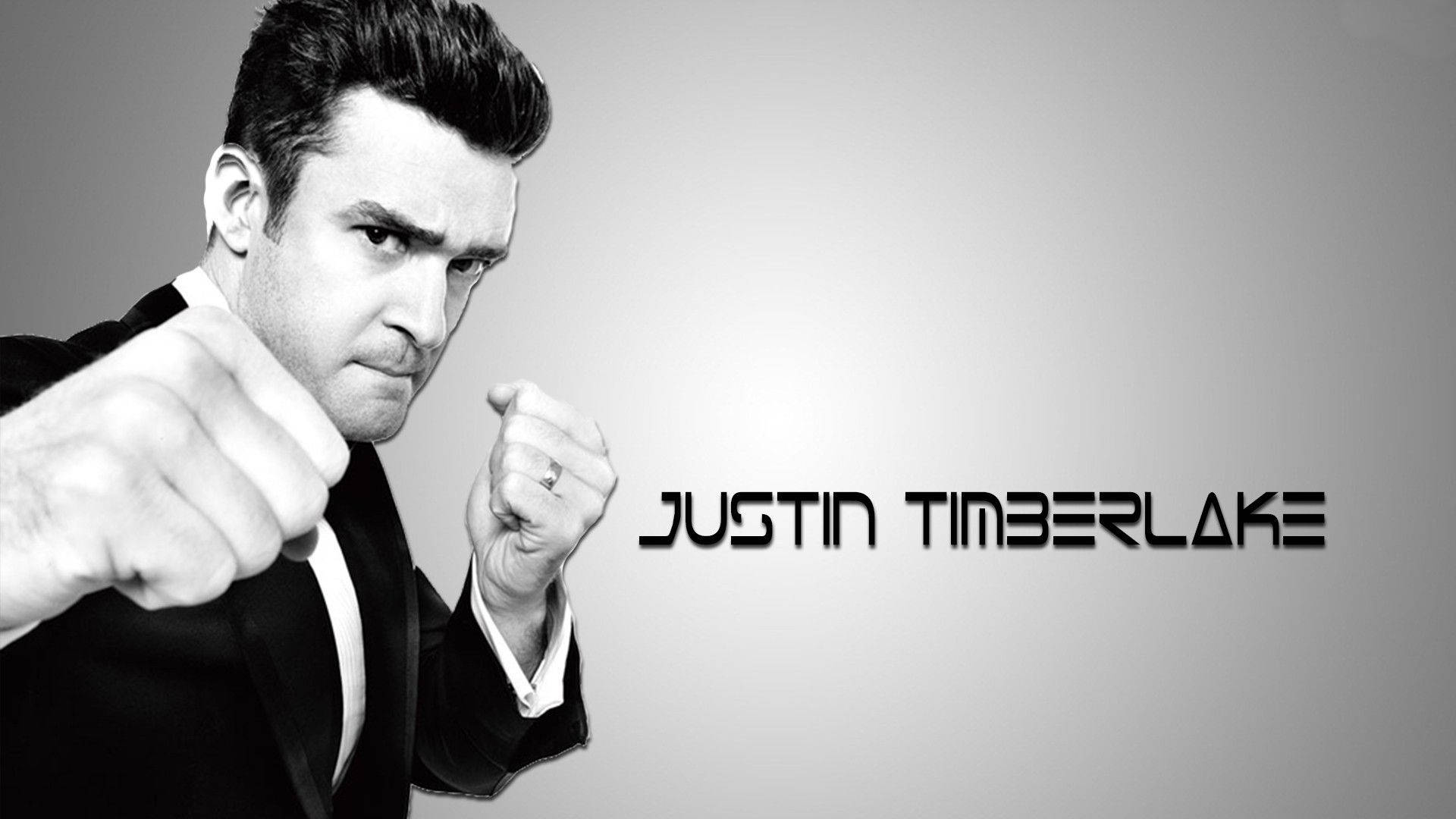 Celebrity 桌布 壁紙 — Justin Timberlake 身穿黑色西裝，在灰色漸變背景前握緊拳頭擺姿勢，他的名字以粗體文字顯示。