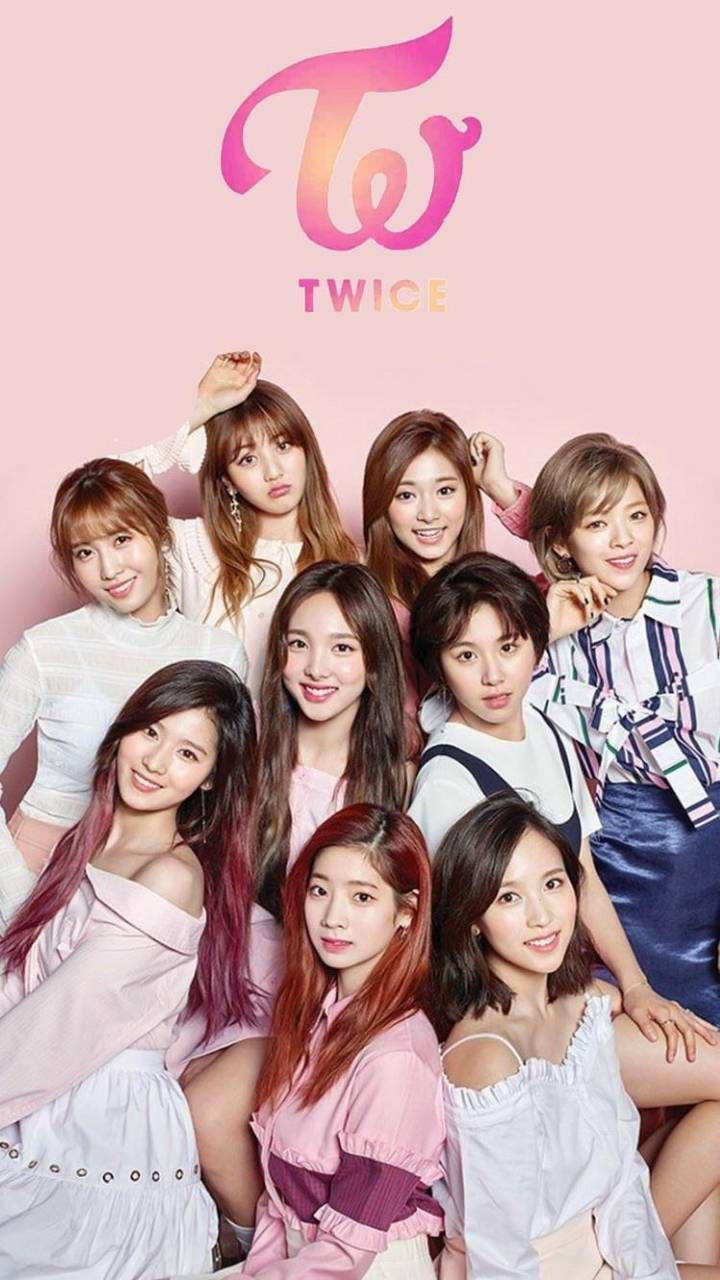 twice 桌布 壁紙 — K-pop 組合 TWICE 的九位成員在柔和的粉紅色背景前愉快地擺姿勢，上方有他們的標誌。