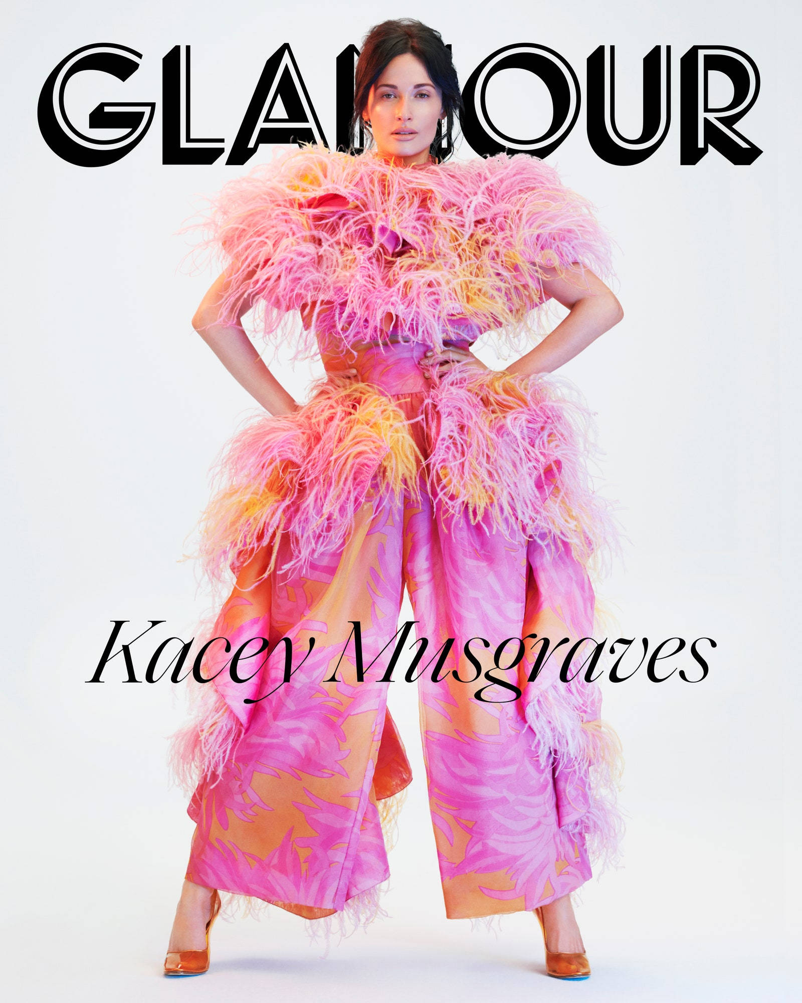 Kacey Musgraves 桌布 壁紙 — Kacey Musgraves 自信地擺姿勢，身穿鮮豔的粉紅色和橙色羽毛長袍，背景是純白色。