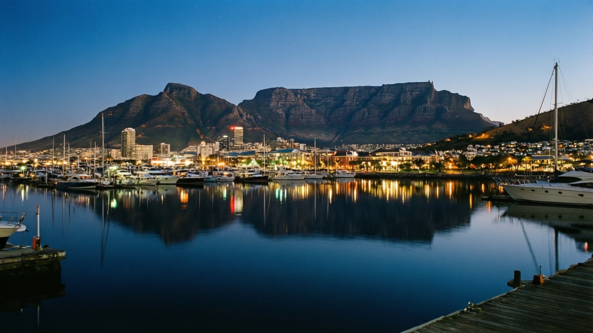 Cape Town Waterfront Night 壁紙 — 開普敦港口黃昏時分，桌山聳立，背後城市燈光閃爍，倒映在平靜的水面上。