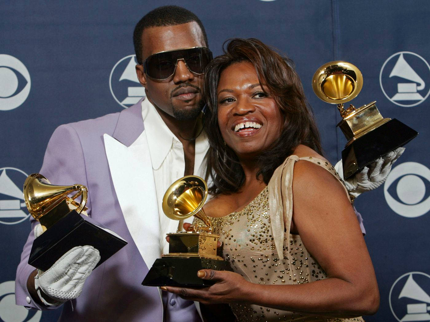 Kanye West Donda 桌布 壁紙 — Kanye West 和他的母親 Donda West 在帶有標誌的藍色背景前自豪地微笑著手持葛萊美獎項。