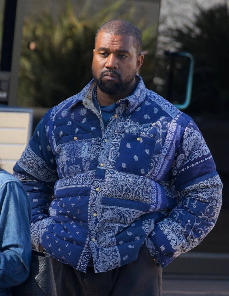 bandana 桌布 壁紙 — Kanye West 在戶外站著，穿著一件大膽的藍色佩斯利絎縫外套，雙手插在口袋裡。