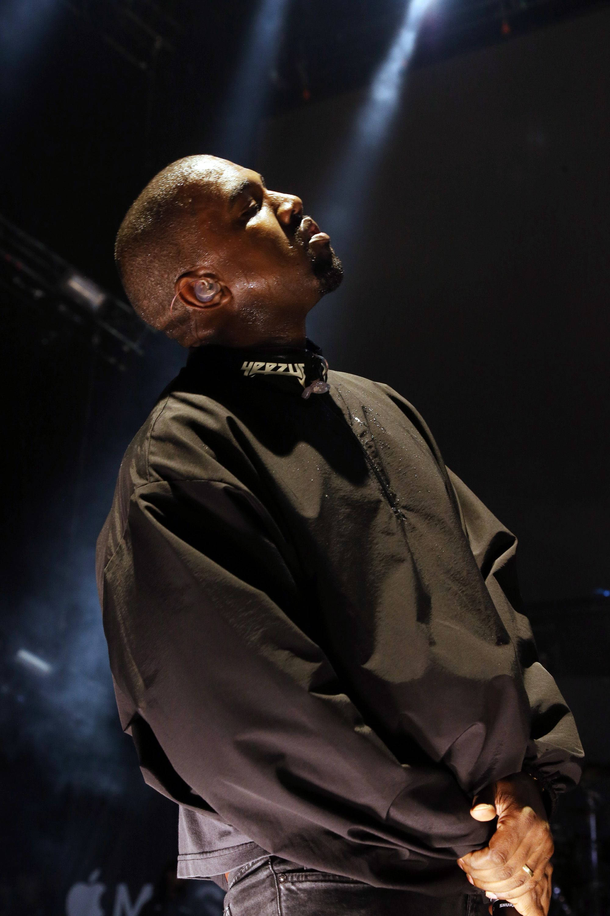 說唱歌手 桌布 壁紙 — Kanye West 在舞台上表演，沐浴在戲劇性的聚光燈下，表情專注而強烈。